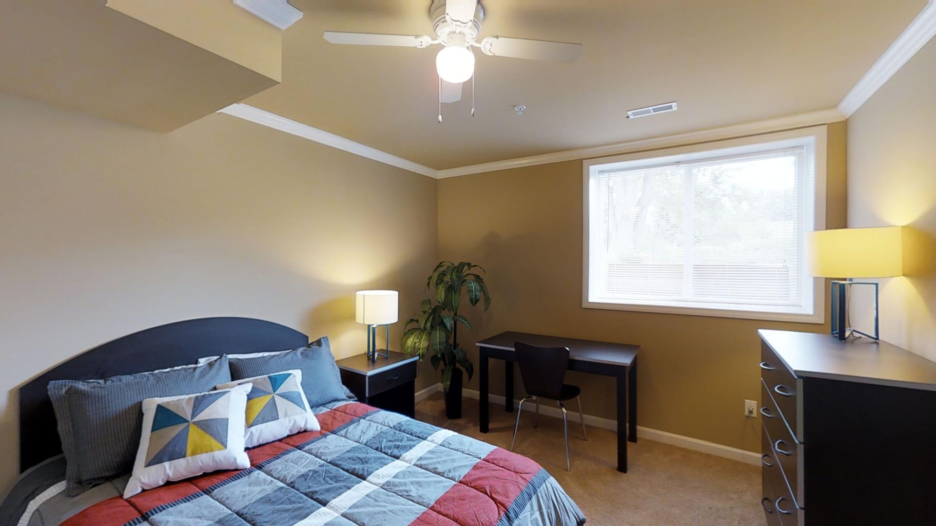 A bedroom with a bed , dresser , desk and ceiling fan.