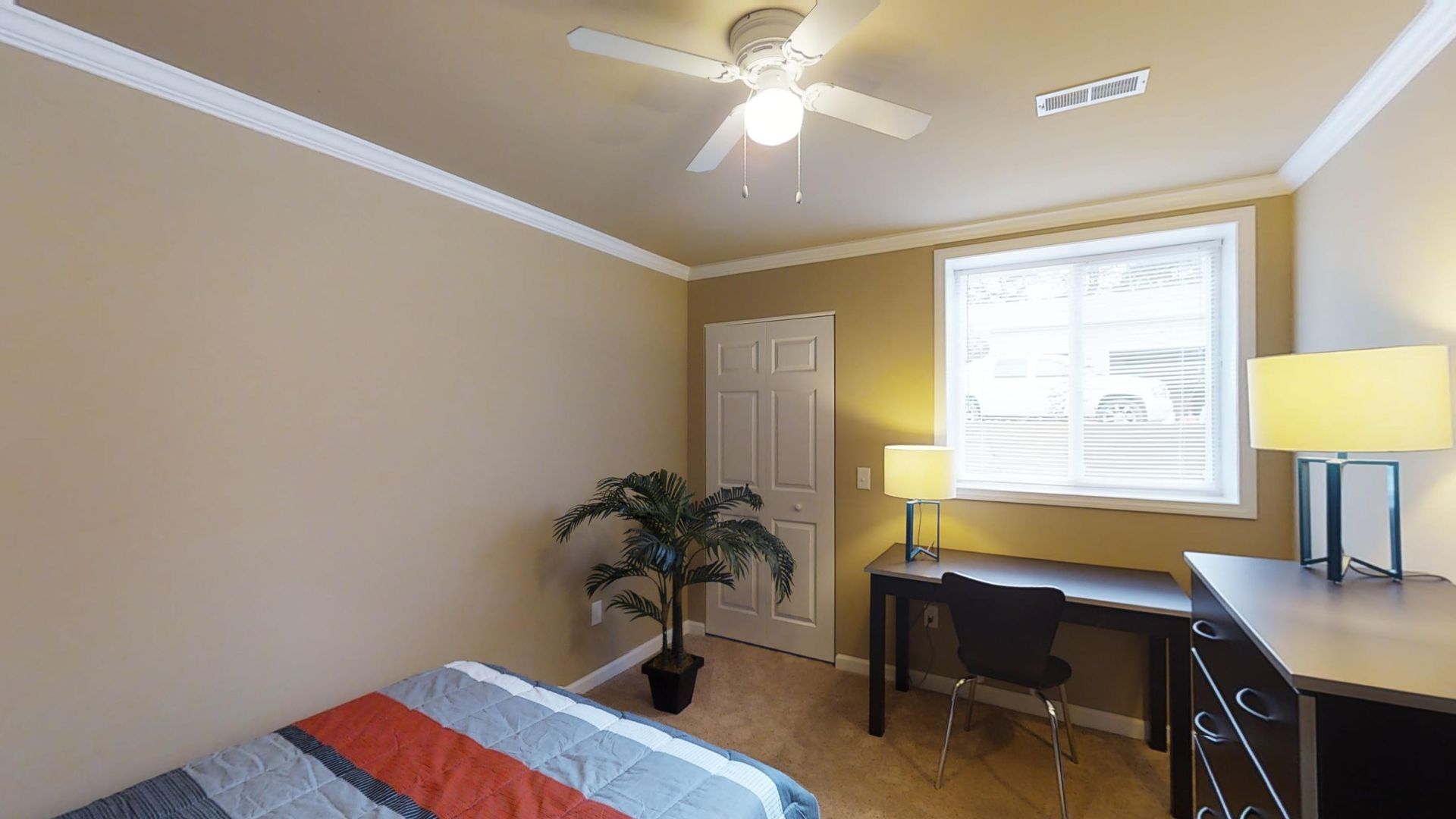A bedroom with a bed , desk , lamp and ceiling fan.