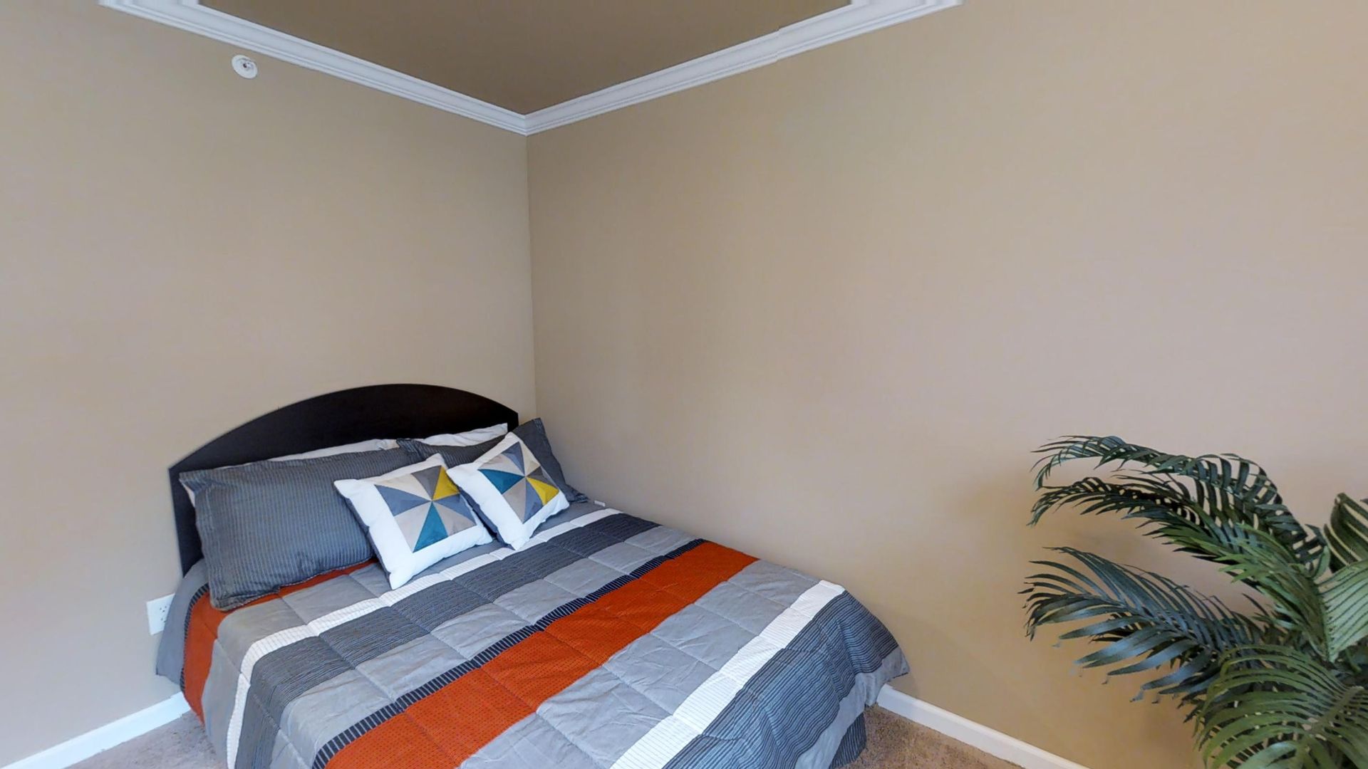 A bedroom with a bed and a plant in the corner.