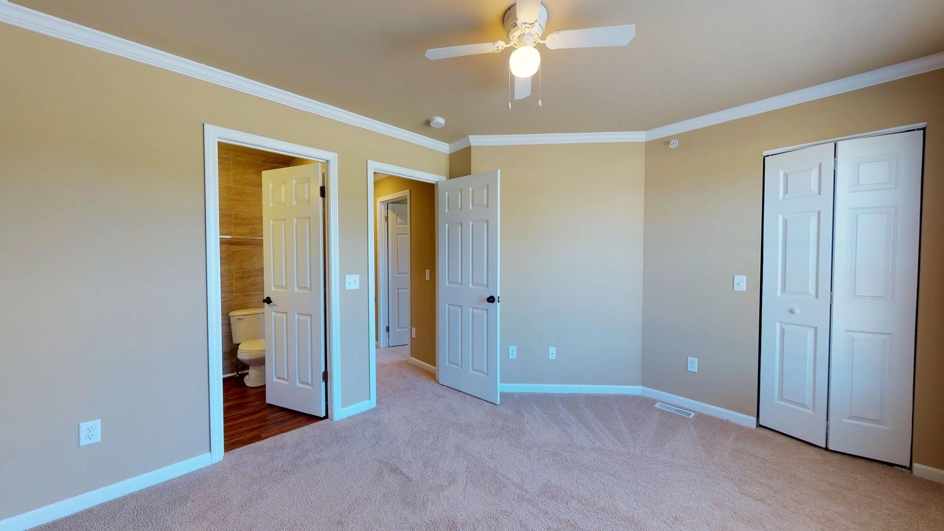 An empty bedroom with a ceiling fan and a toilet.