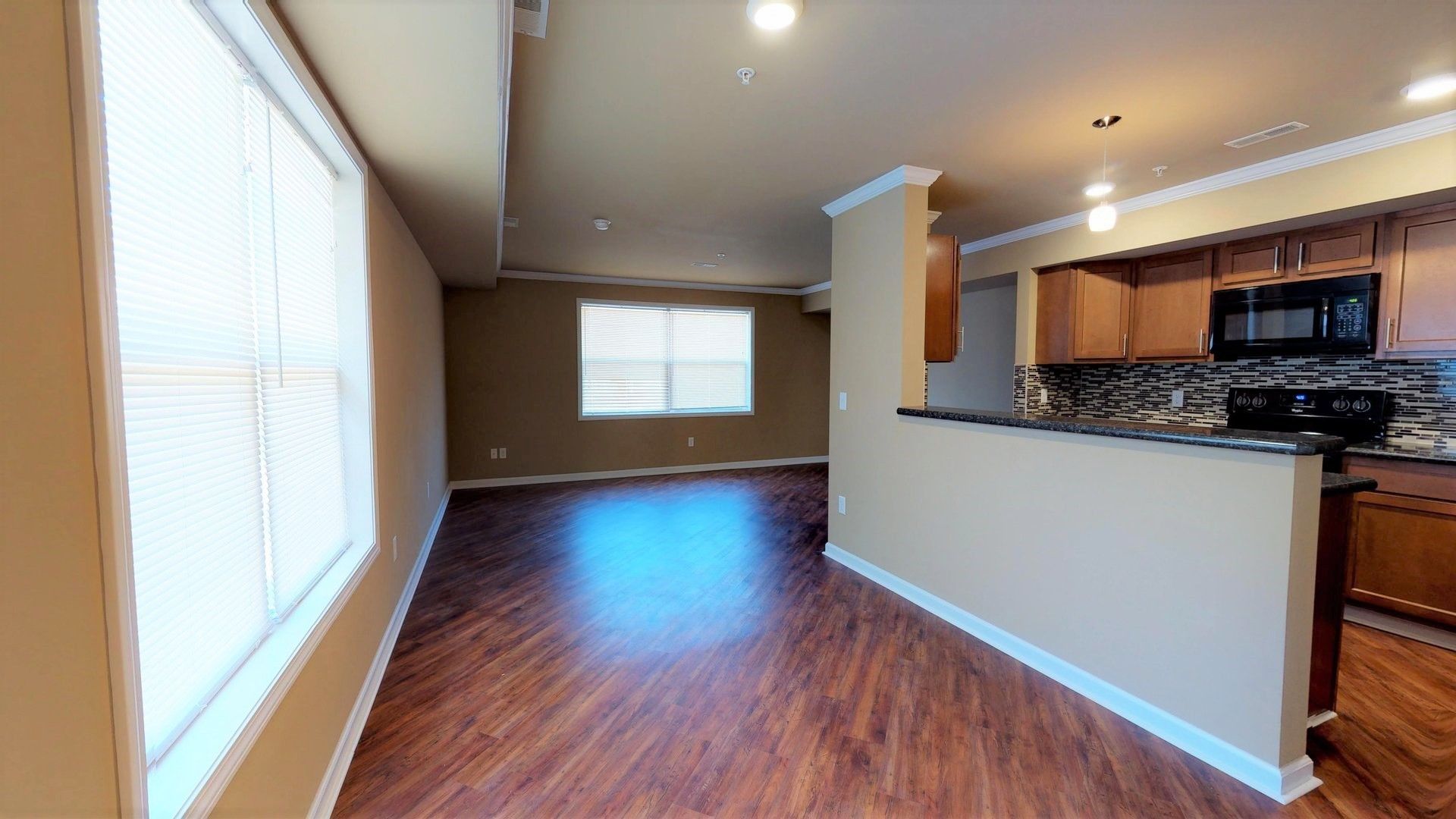 A living room with hardwood floors and a kitchen in the background.