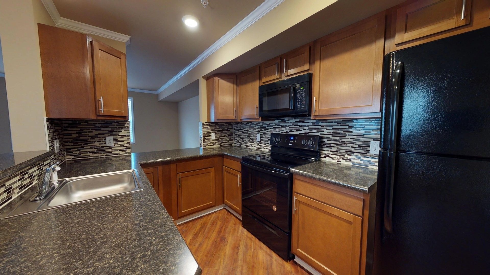 A kitchen with wooden cabinets , granite counter tops , a stove , microwave , refrigerator and sink.