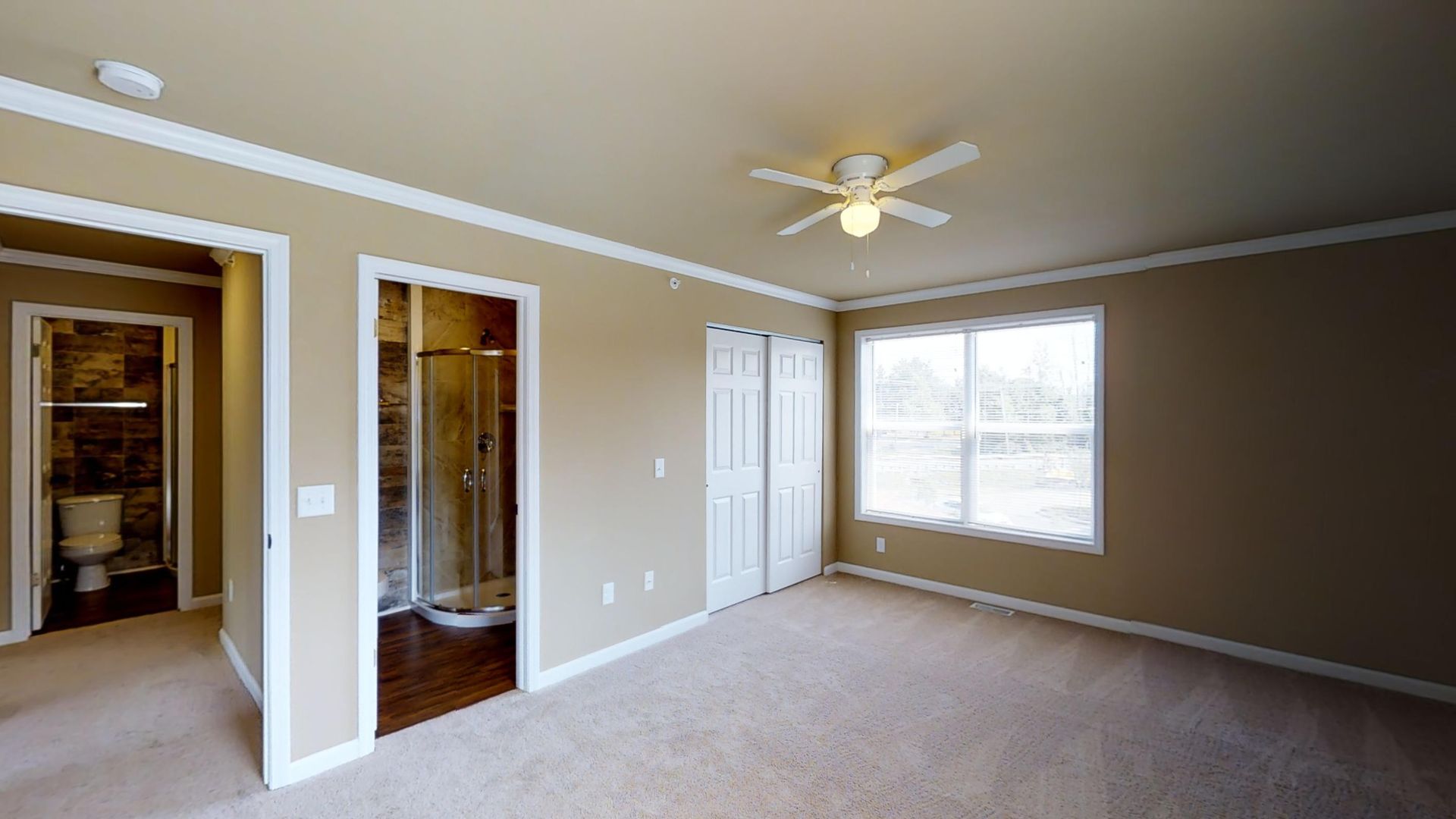 An empty bedroom with a ceiling fan and a bathroom.