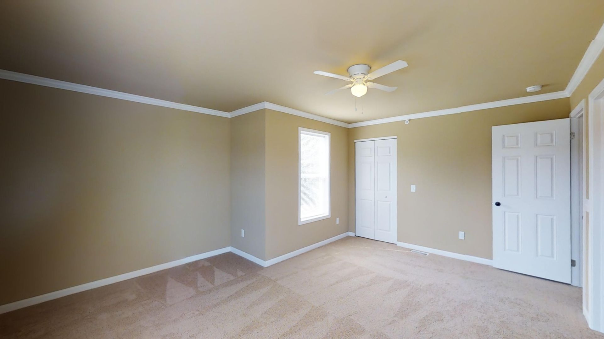 An empty bedroom with a ceiling fan and a window.