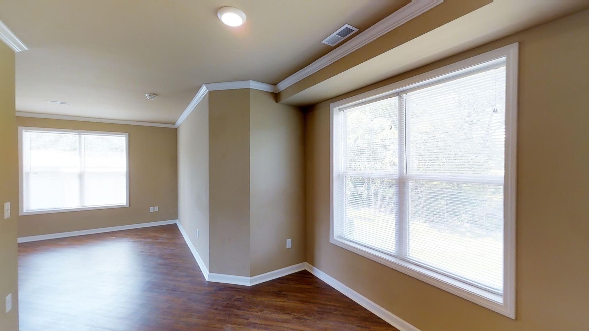 An empty room with hardwood floors and two windows.