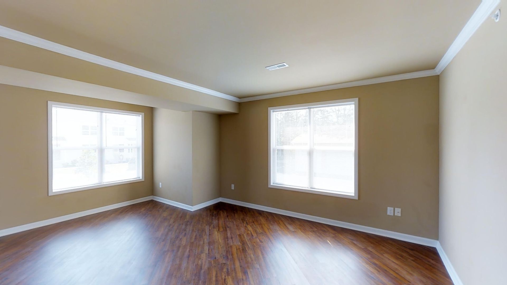 An empty living room with hardwood floors and two windows.