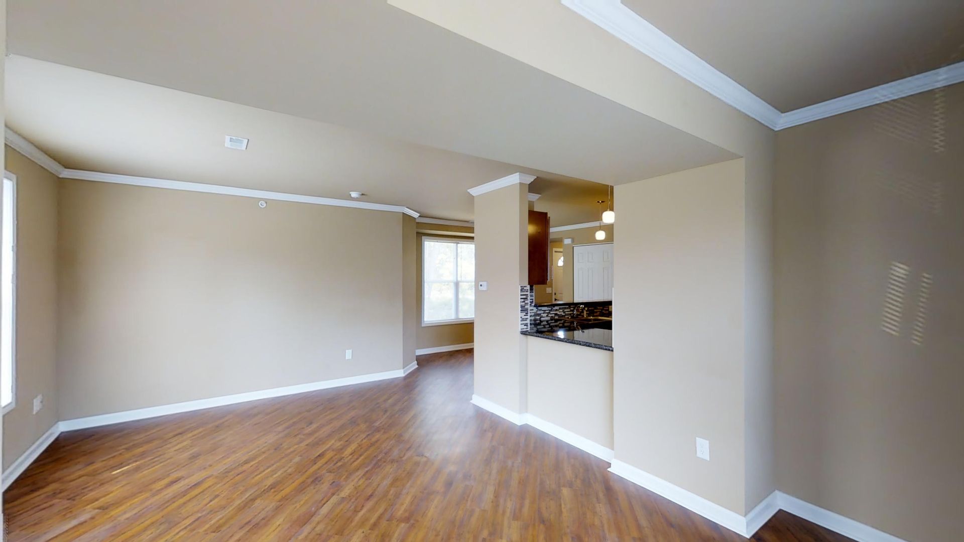 An empty living room with hardwood floors and beige walls.