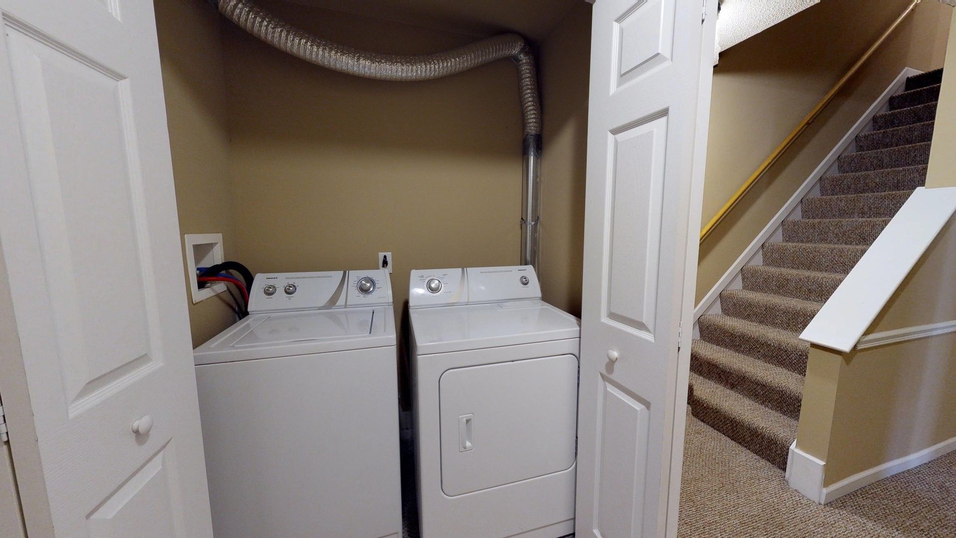 A laundry room with a washer and dryer and stairs.