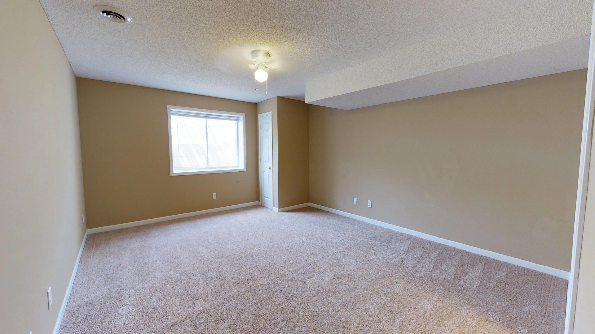 An empty room with a carpeted floor and a window.