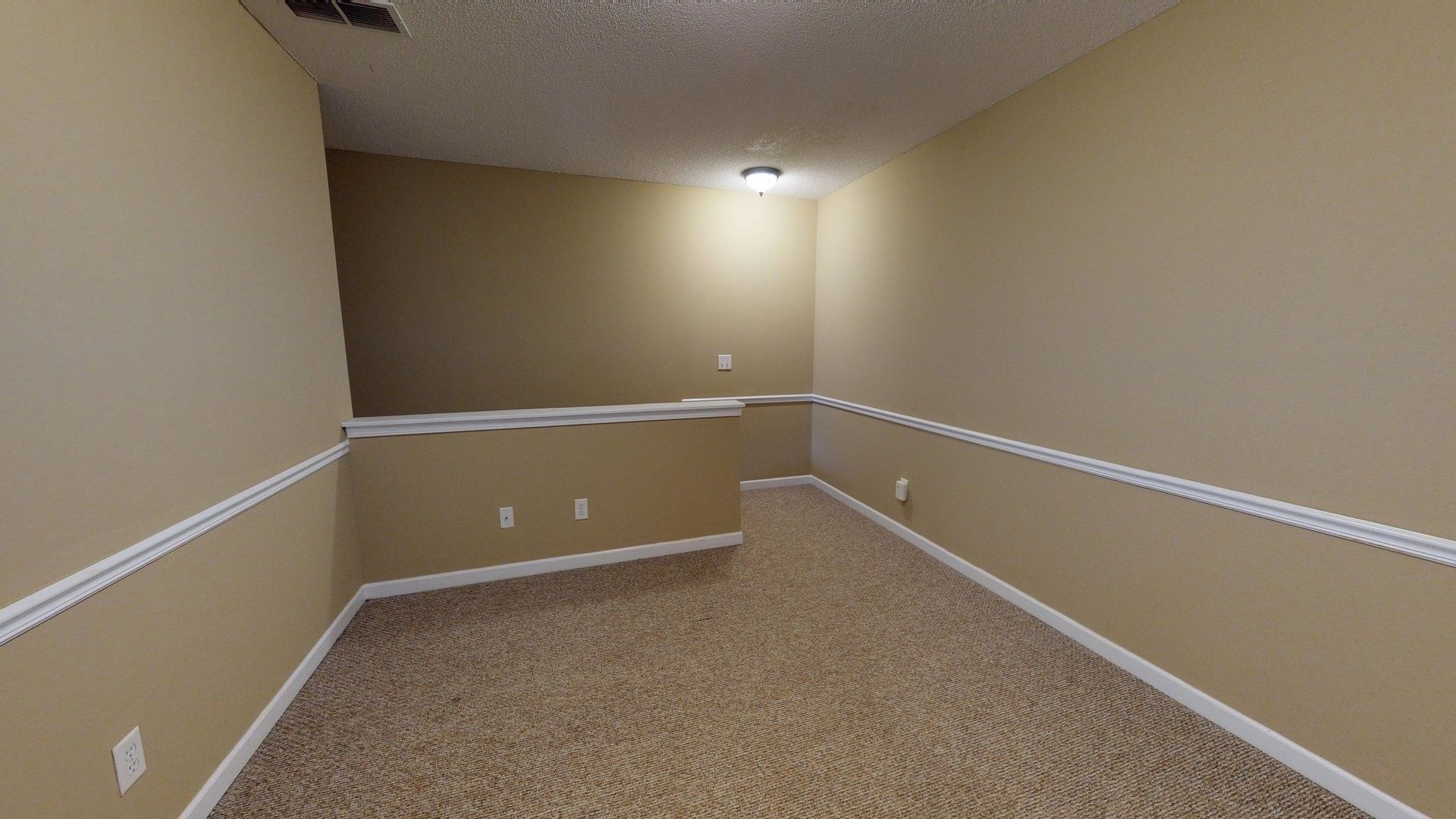 An empty room with a carpeted floor and tan walls.