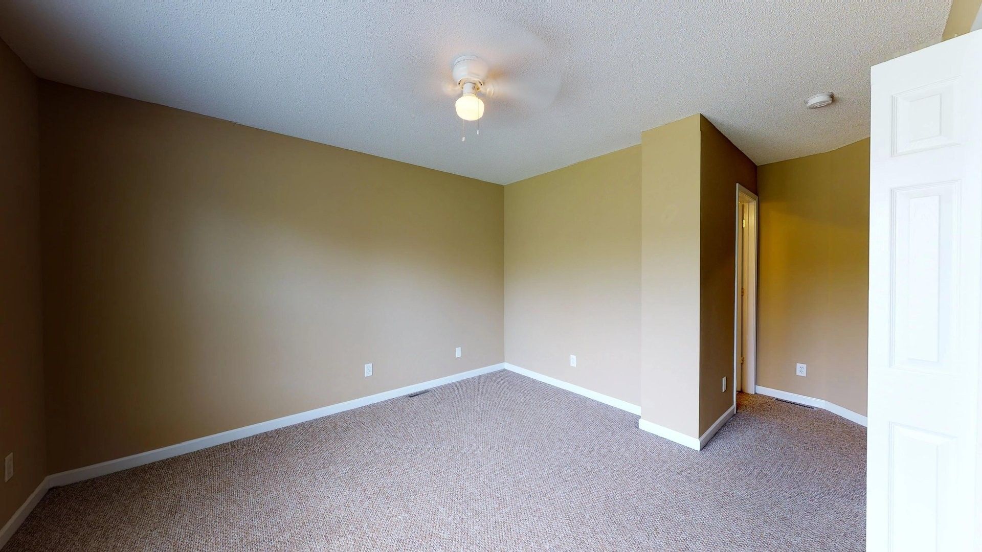 An empty bedroom with a ceiling fan and a carpeted floor.