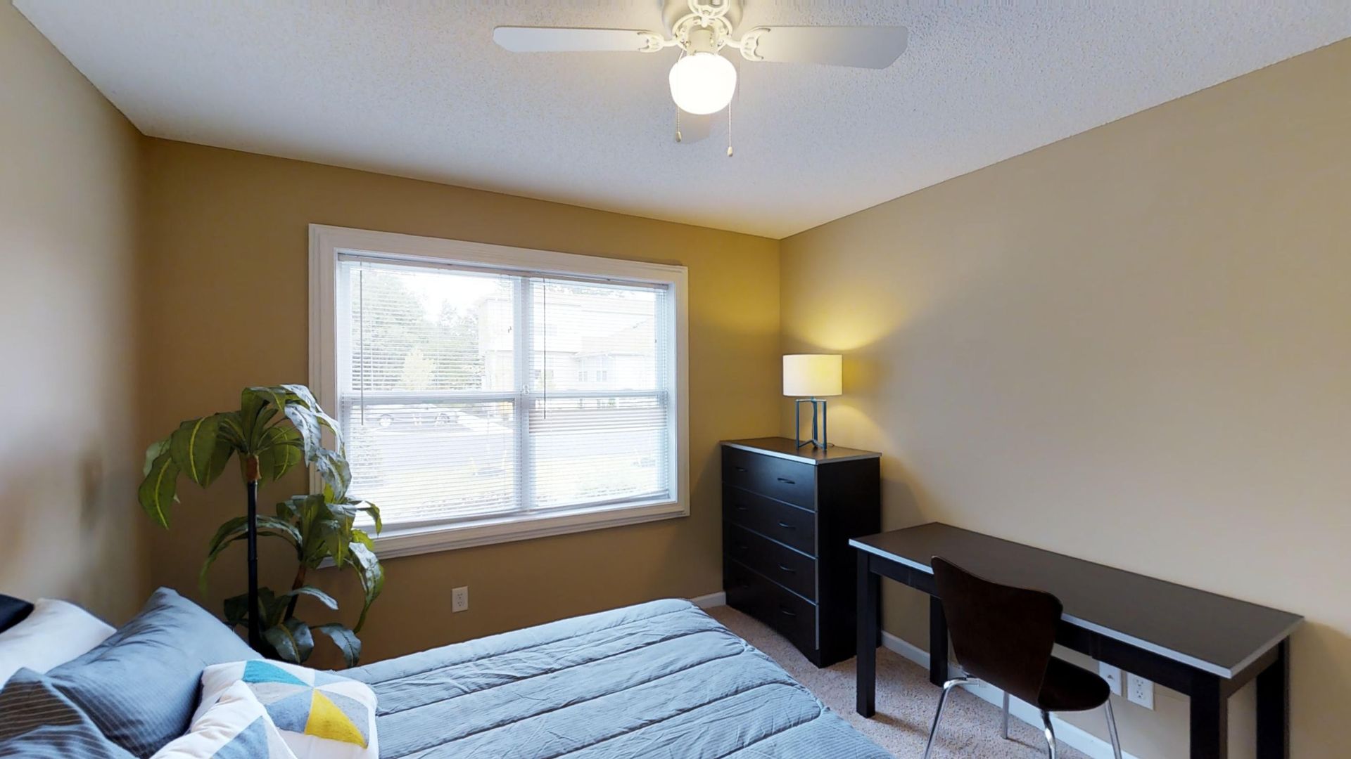 A bedroom with a bed , desk , dresser and ceiling fan.