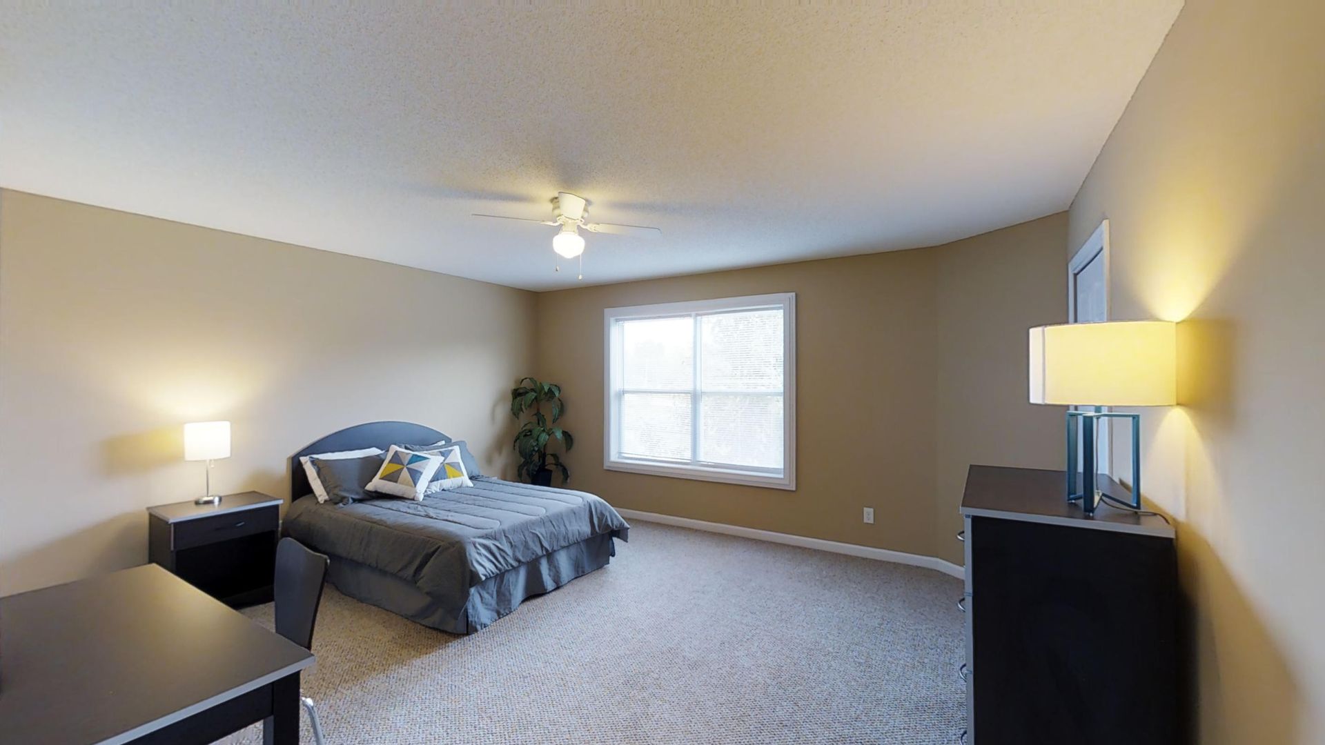 A bedroom with a bed , dresser , nightstand , lamp and window.
