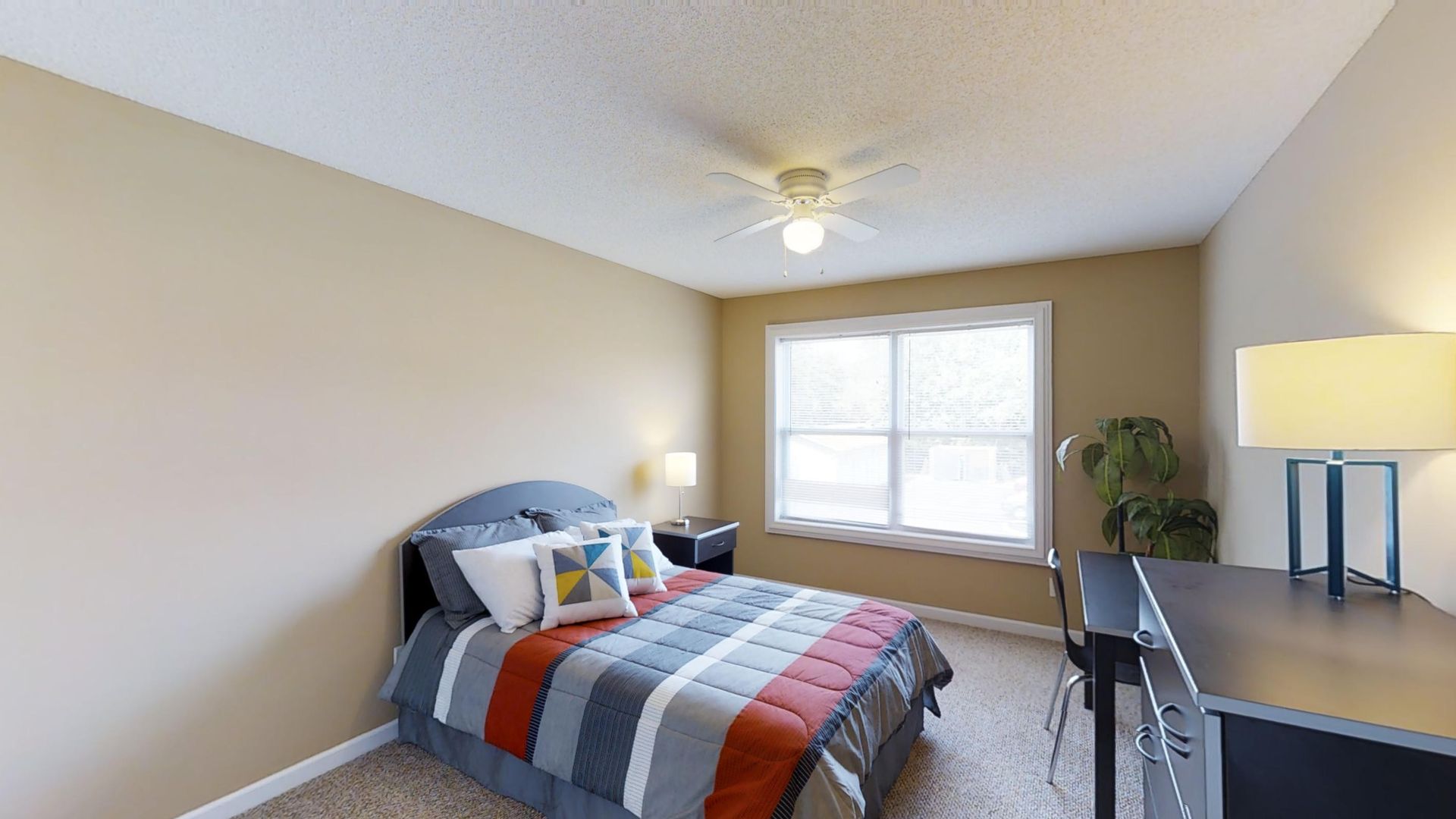 A bedroom with a bed , desk , lamp and window.