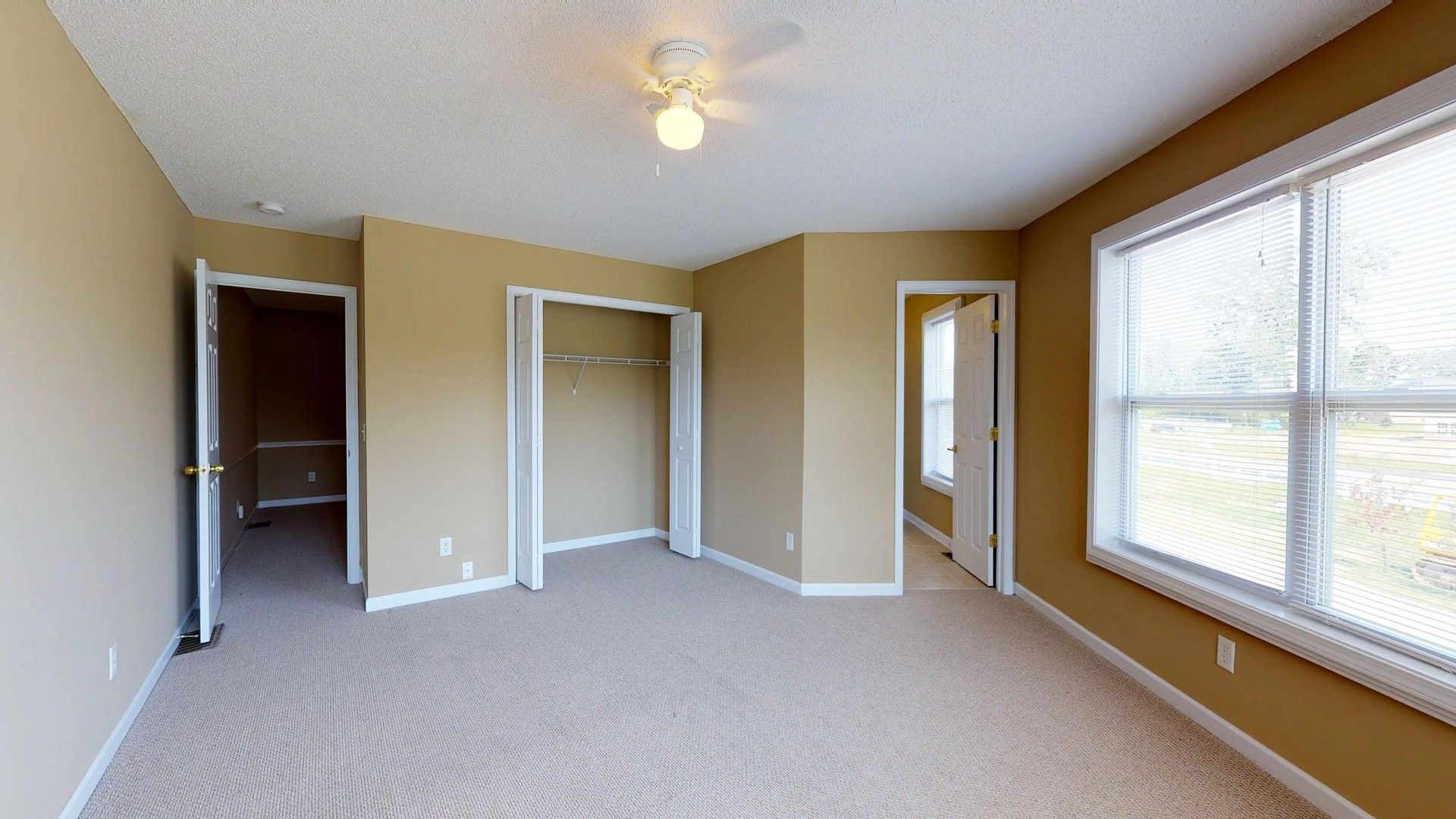 An empty bedroom with a ceiling fan and two windows.