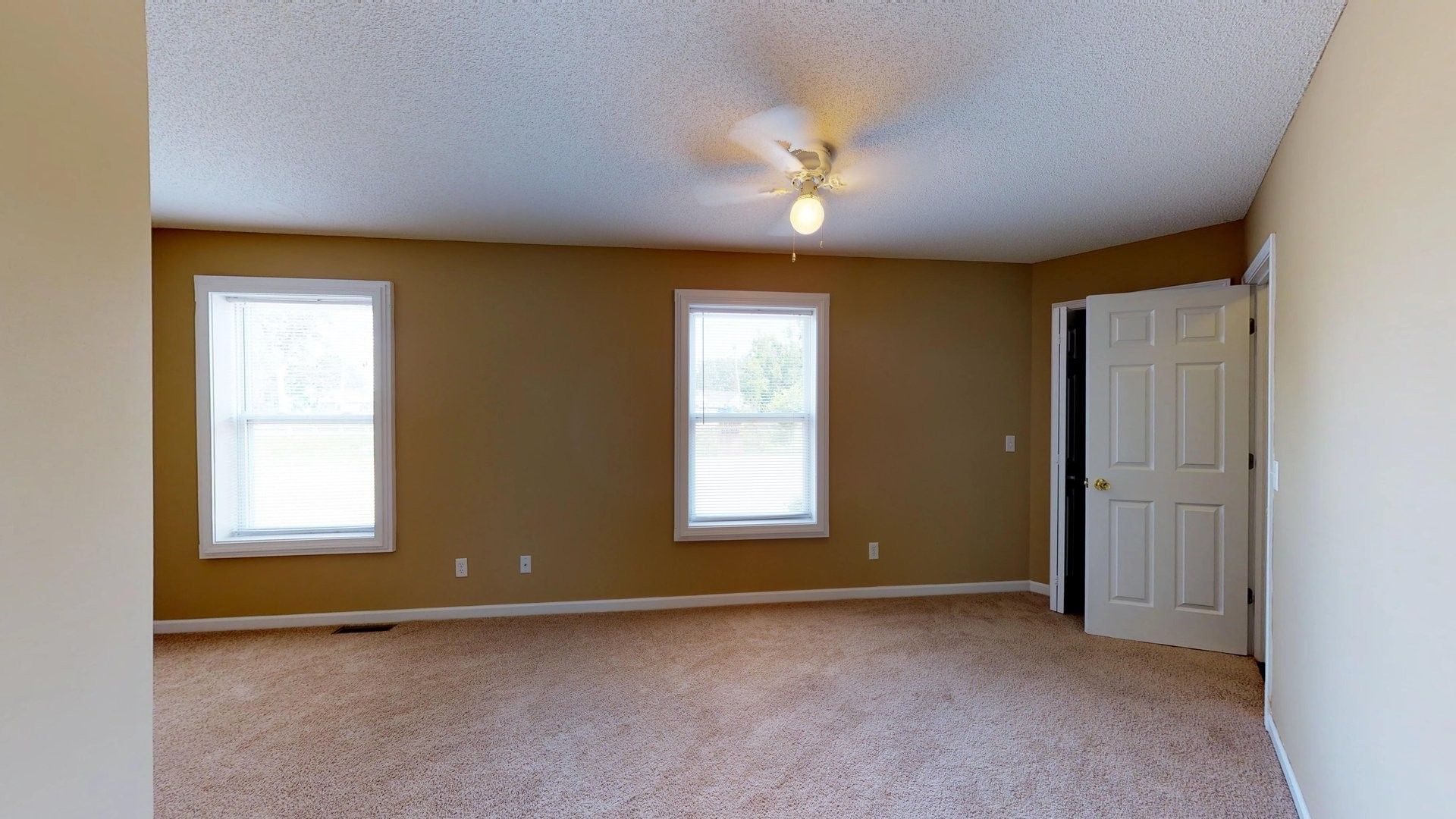 An empty bedroom with a ceiling fan and three windows.