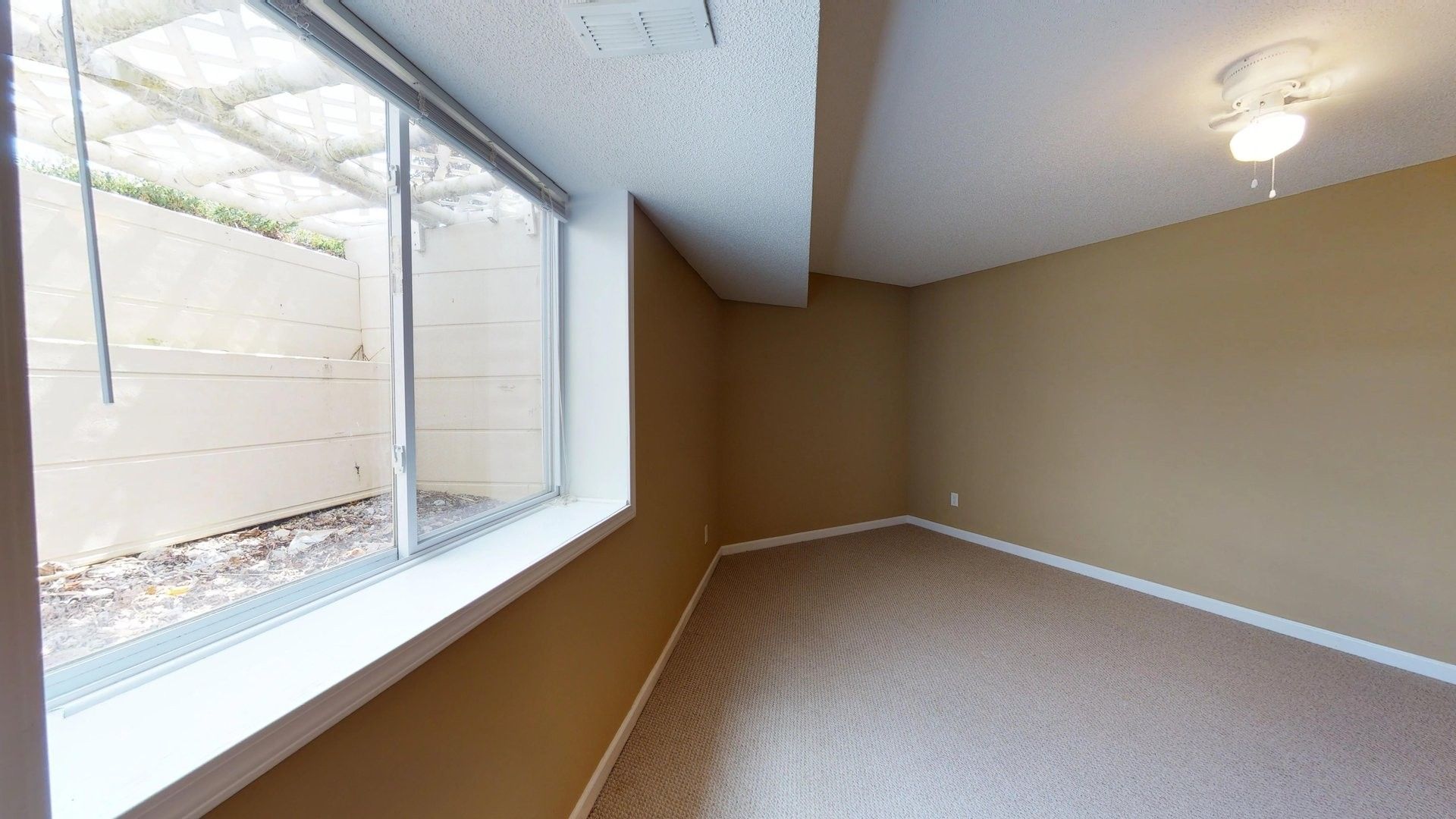 An empty room with a large window and a ceiling fan.