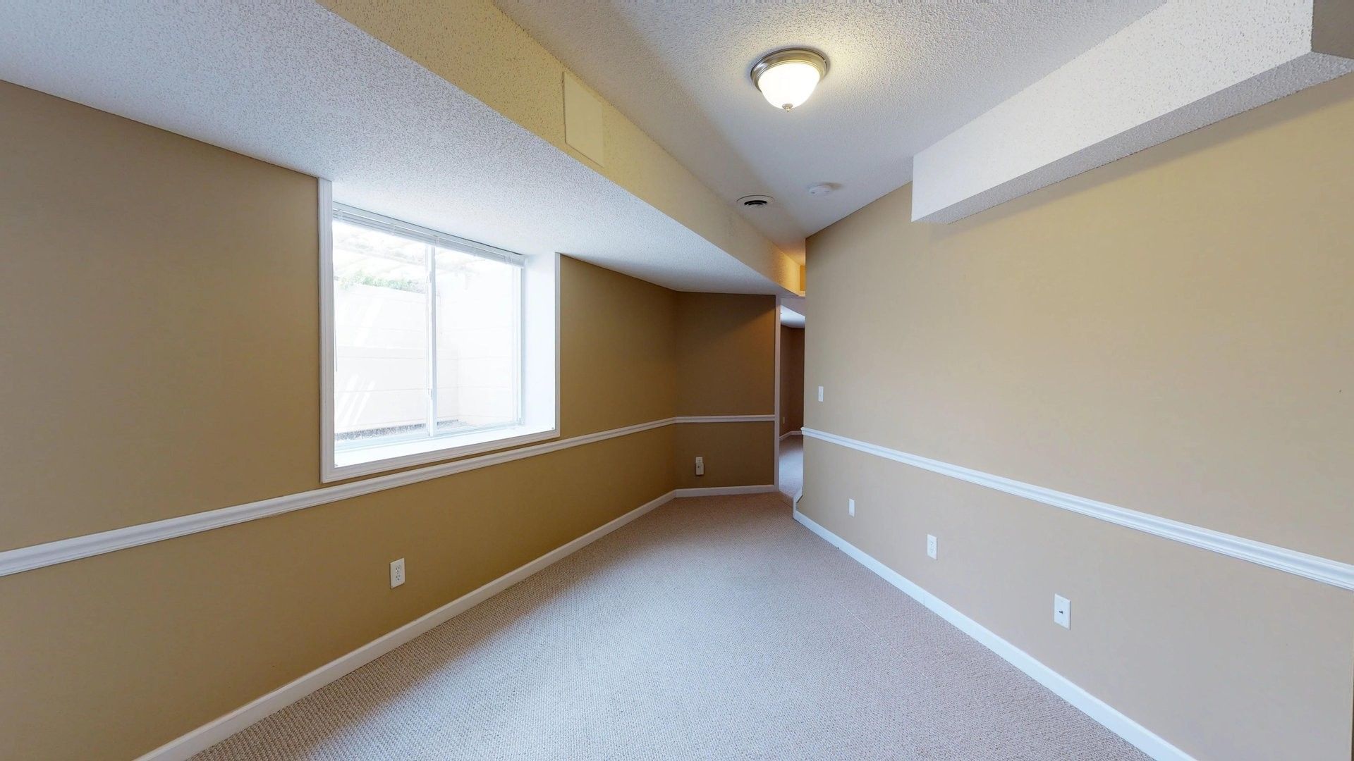 An empty basement with tan walls and a window.