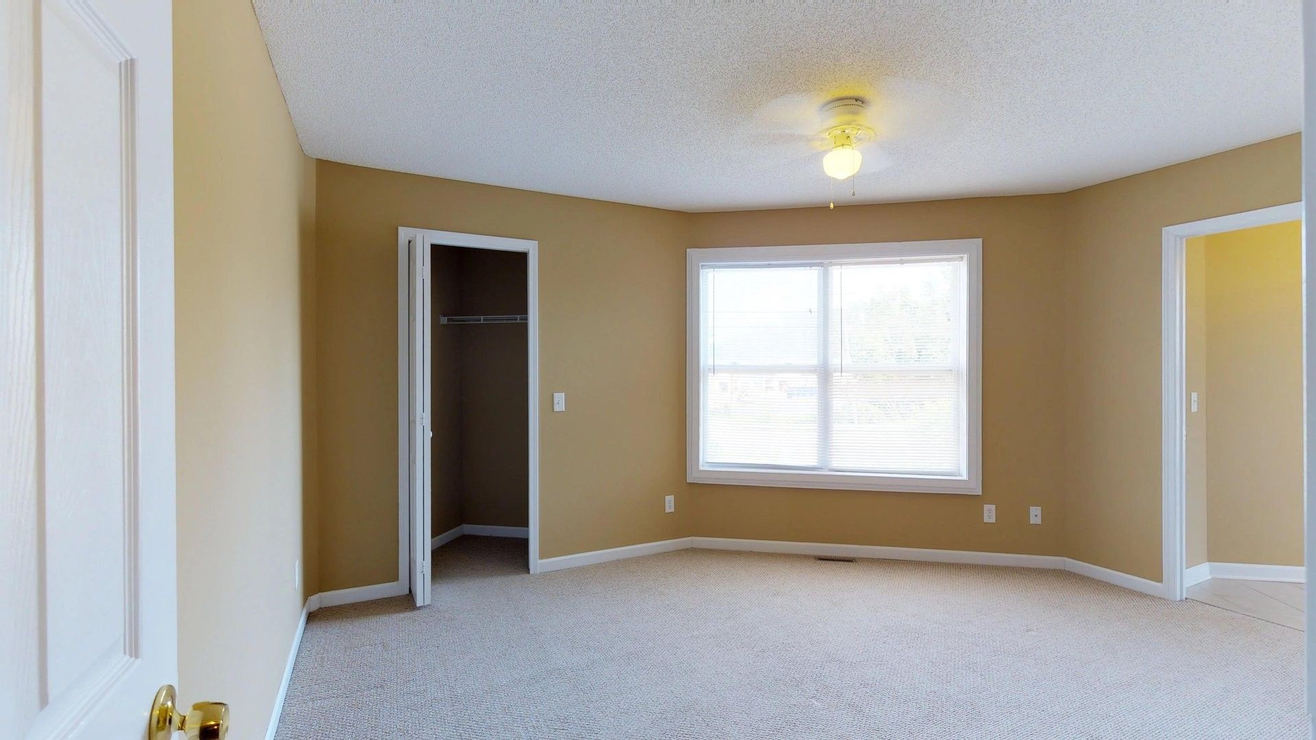 An empty bedroom with a large window and a ceiling fan.