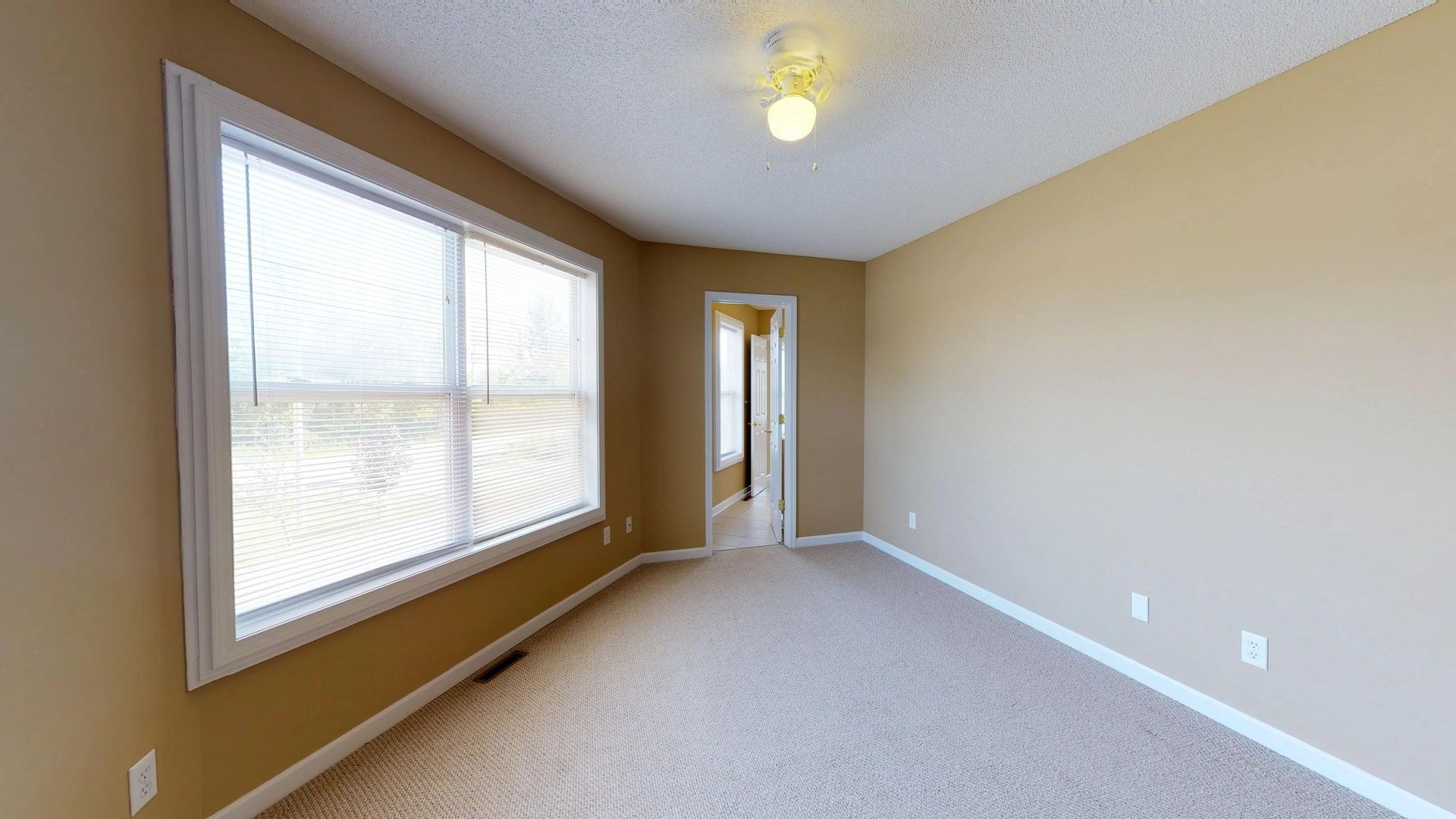 An empty room with a large window and a ceiling fan.