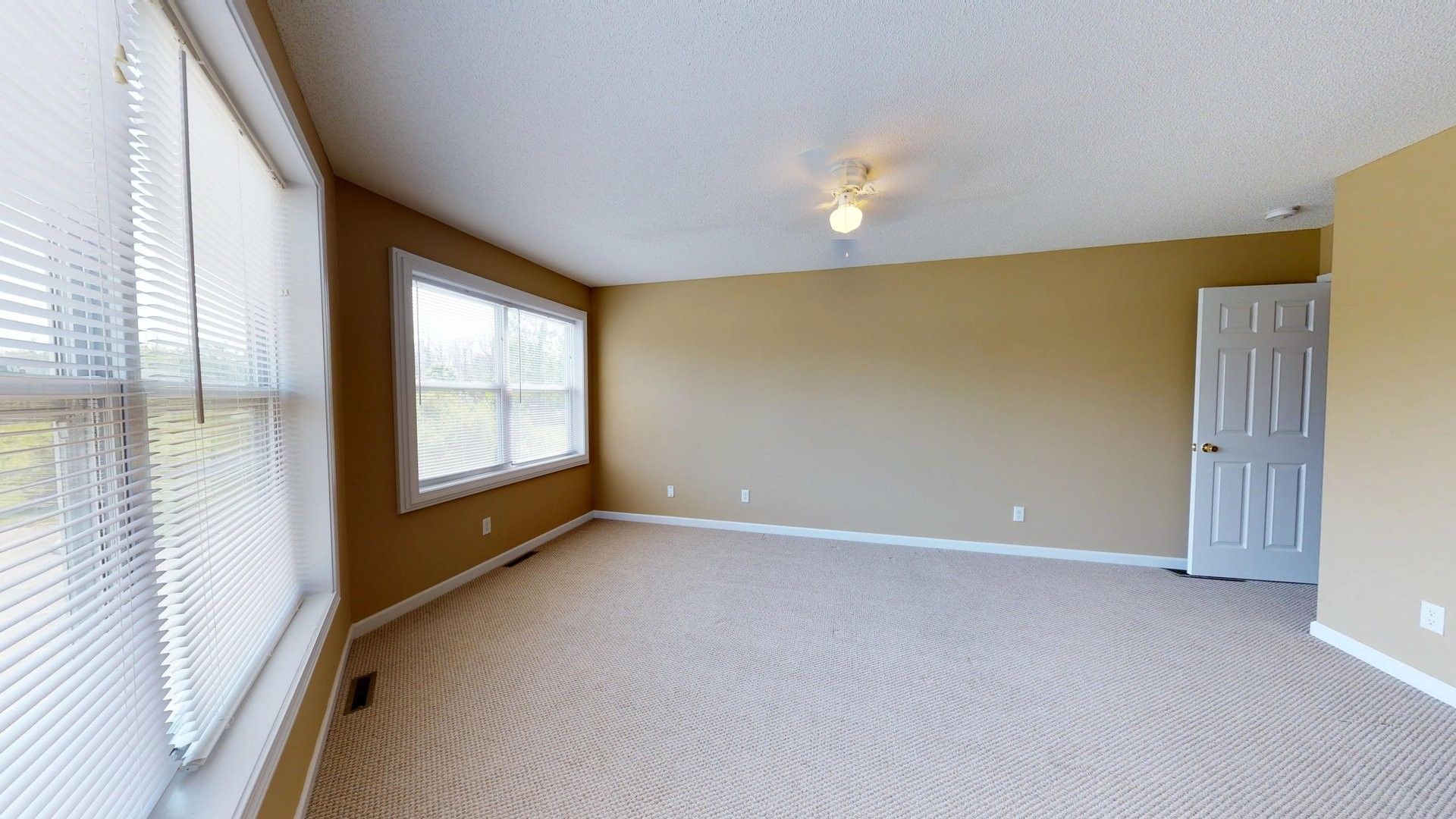 An empty living room with a lot of windows and a ceiling fan.