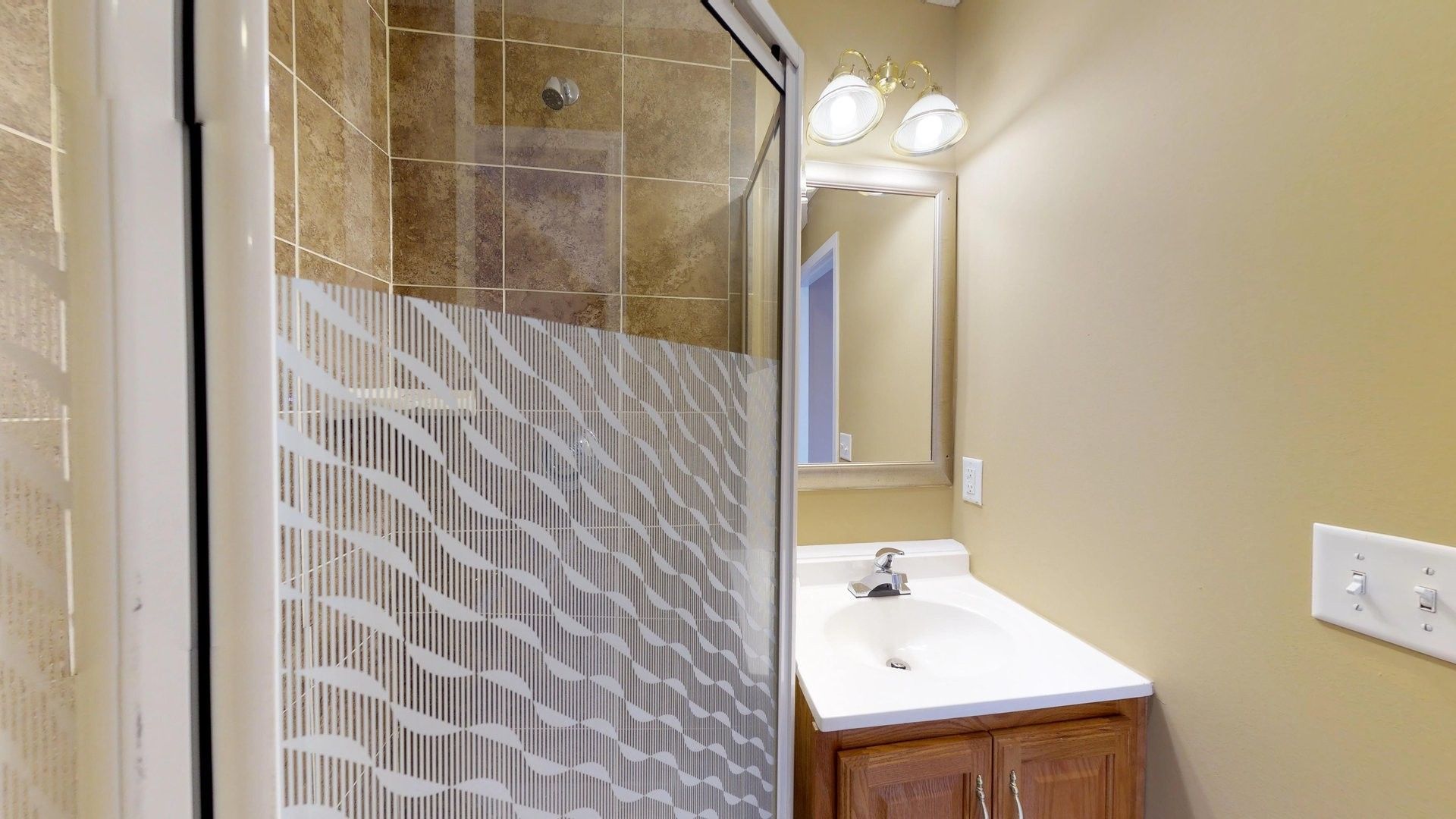 A bathroom with a sink , mirror and shower stall.