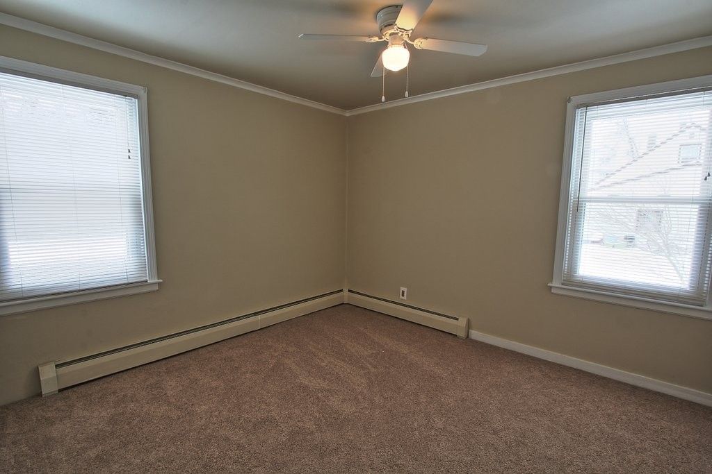 An empty room with a ceiling fan and two windows.