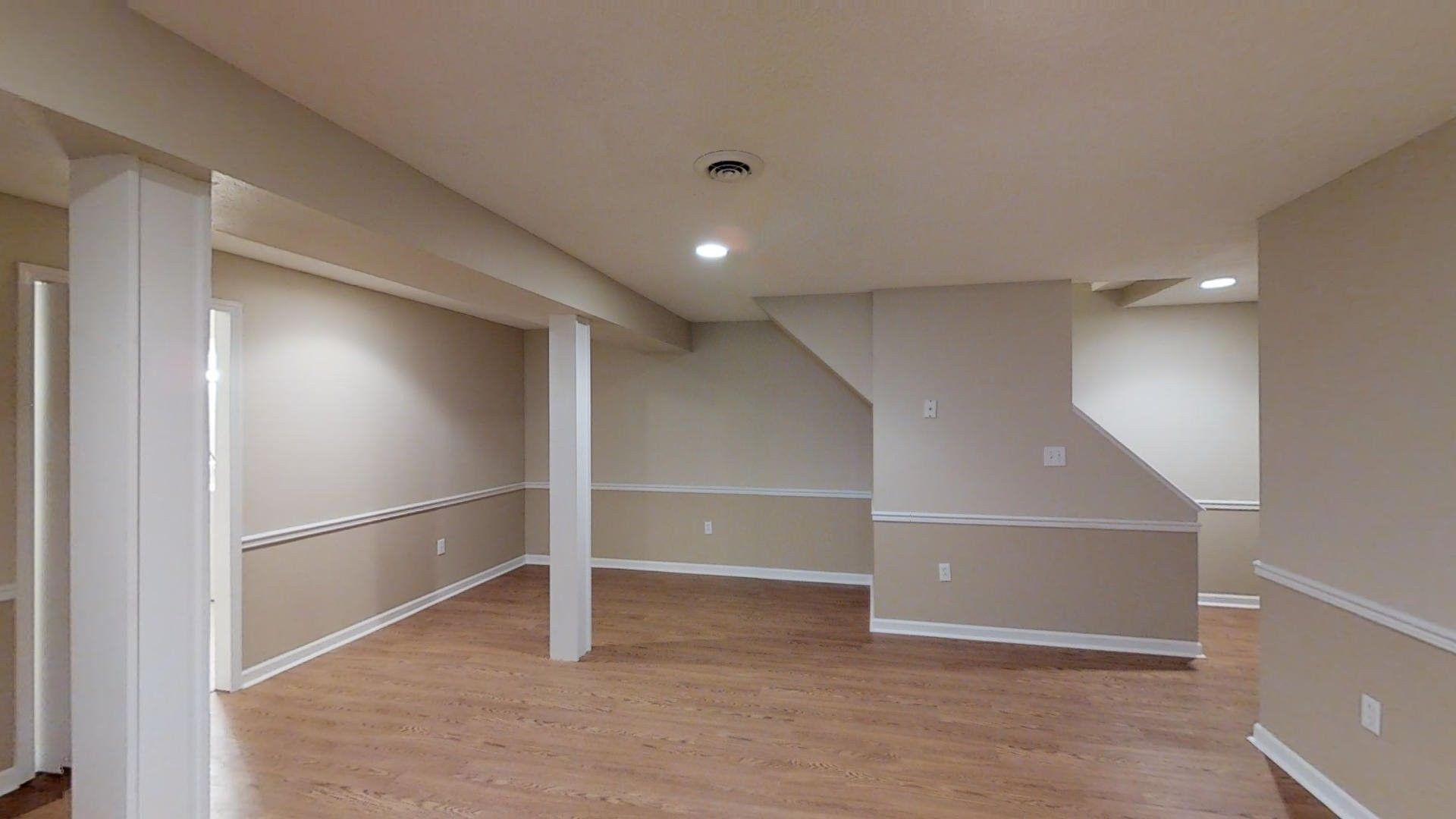 An empty basement with hardwood floors and beige walls.