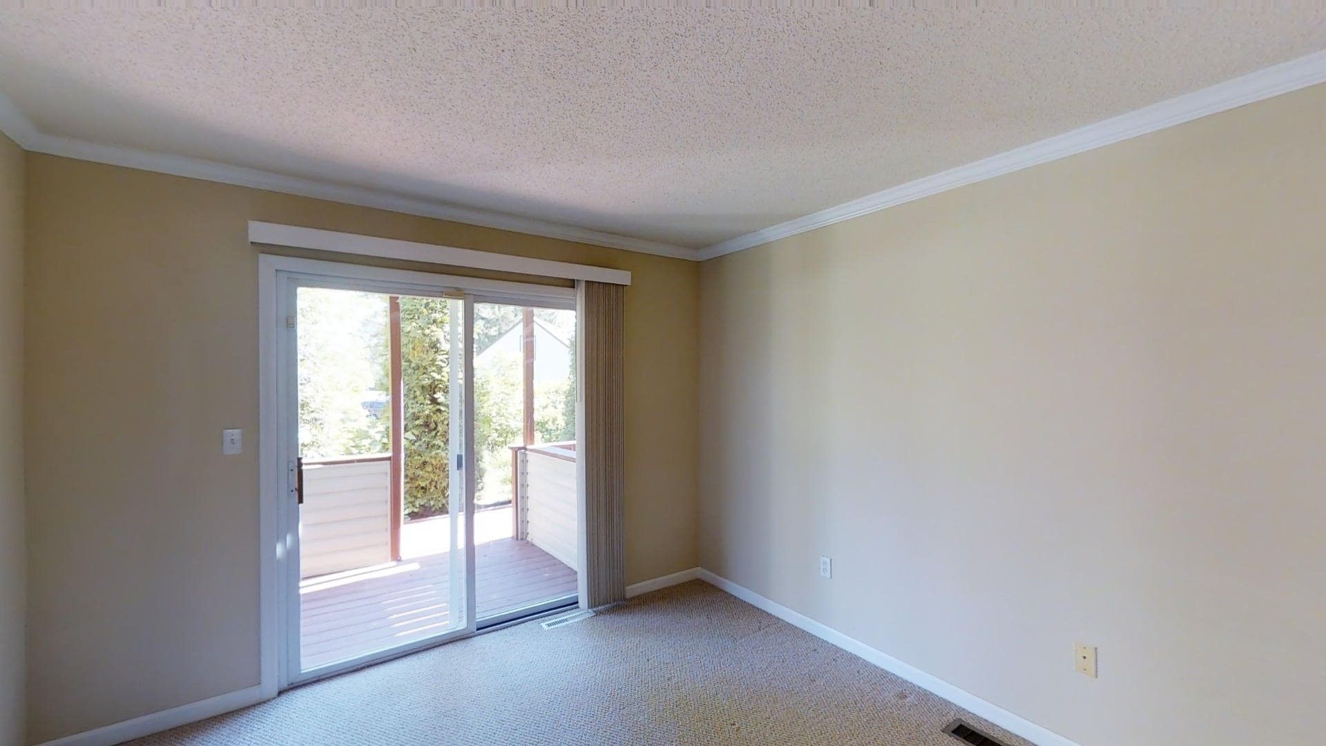 An empty living room with a sliding glass door leading to a balcony.