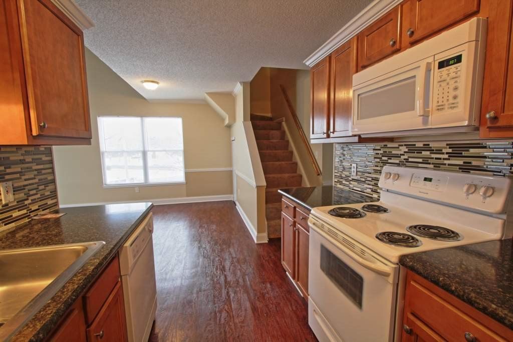 A kitchen with a stove , sink , microwave and stairs.