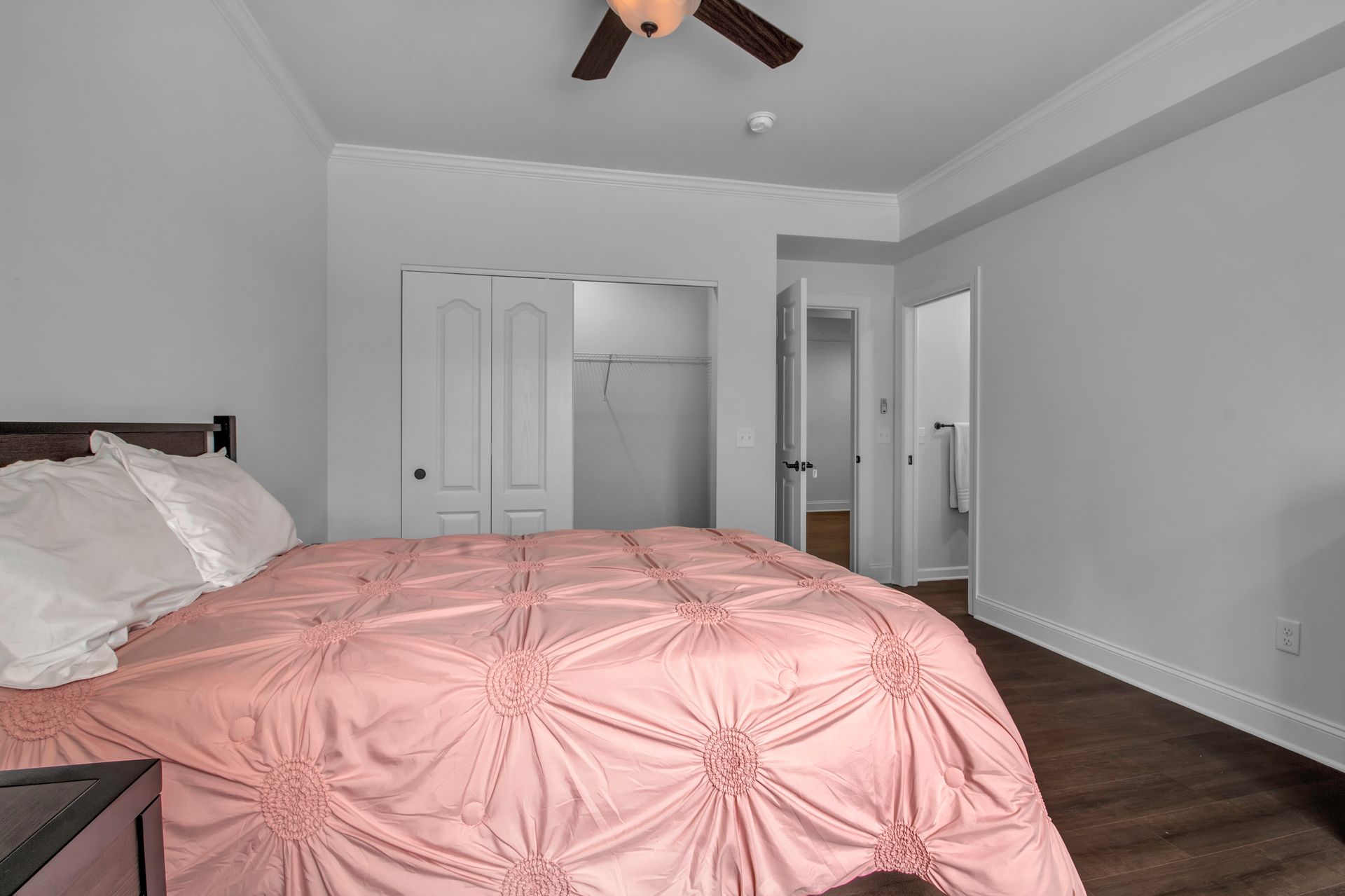 A bedroom with a pink comforter and a ceiling fan.