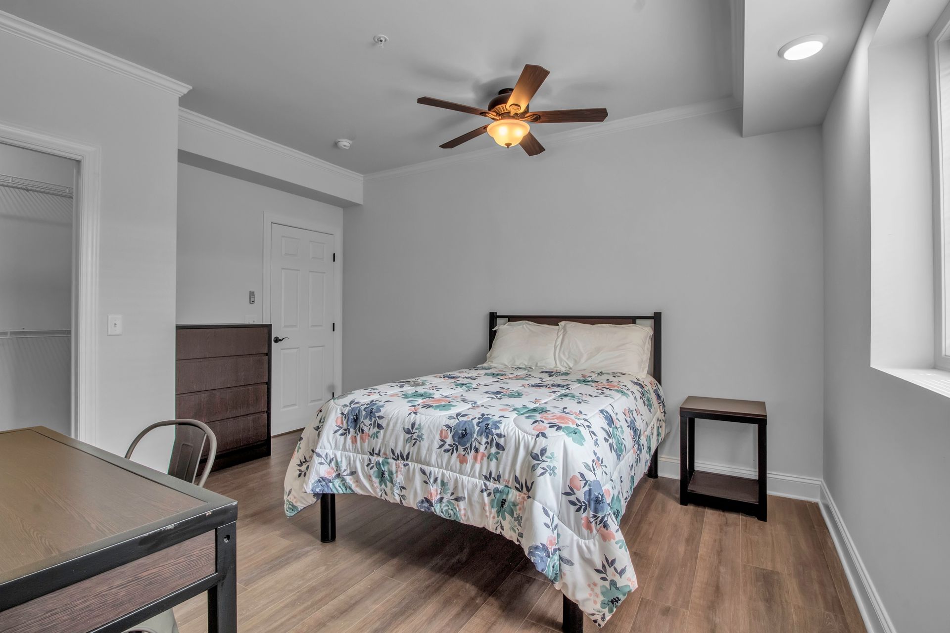 A bedroom with a bed , nightstand , desk and ceiling fan.