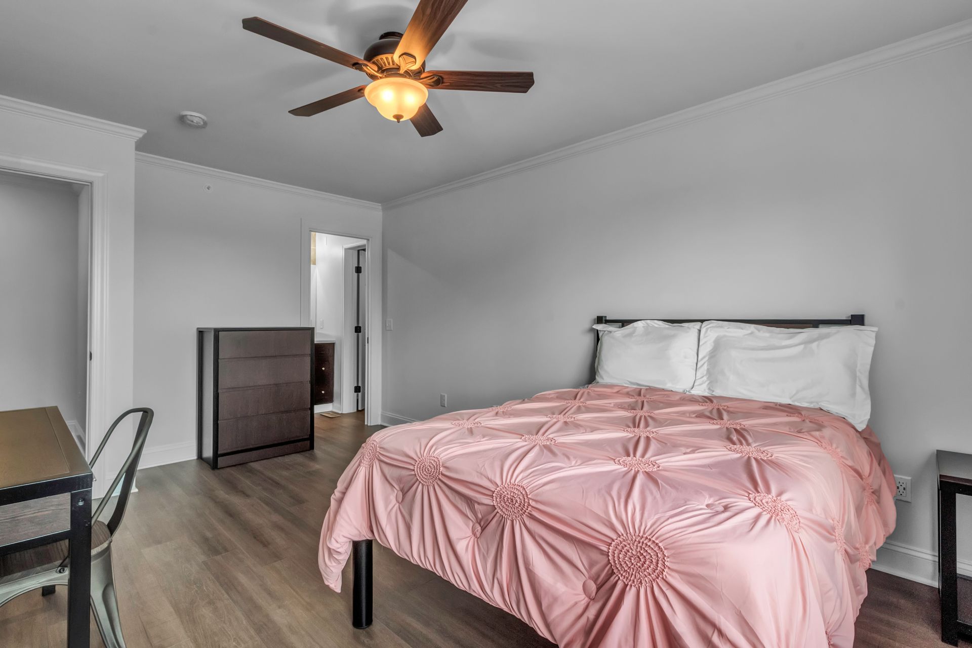 A bedroom with a bed , desk , chairs and a ceiling fan.
