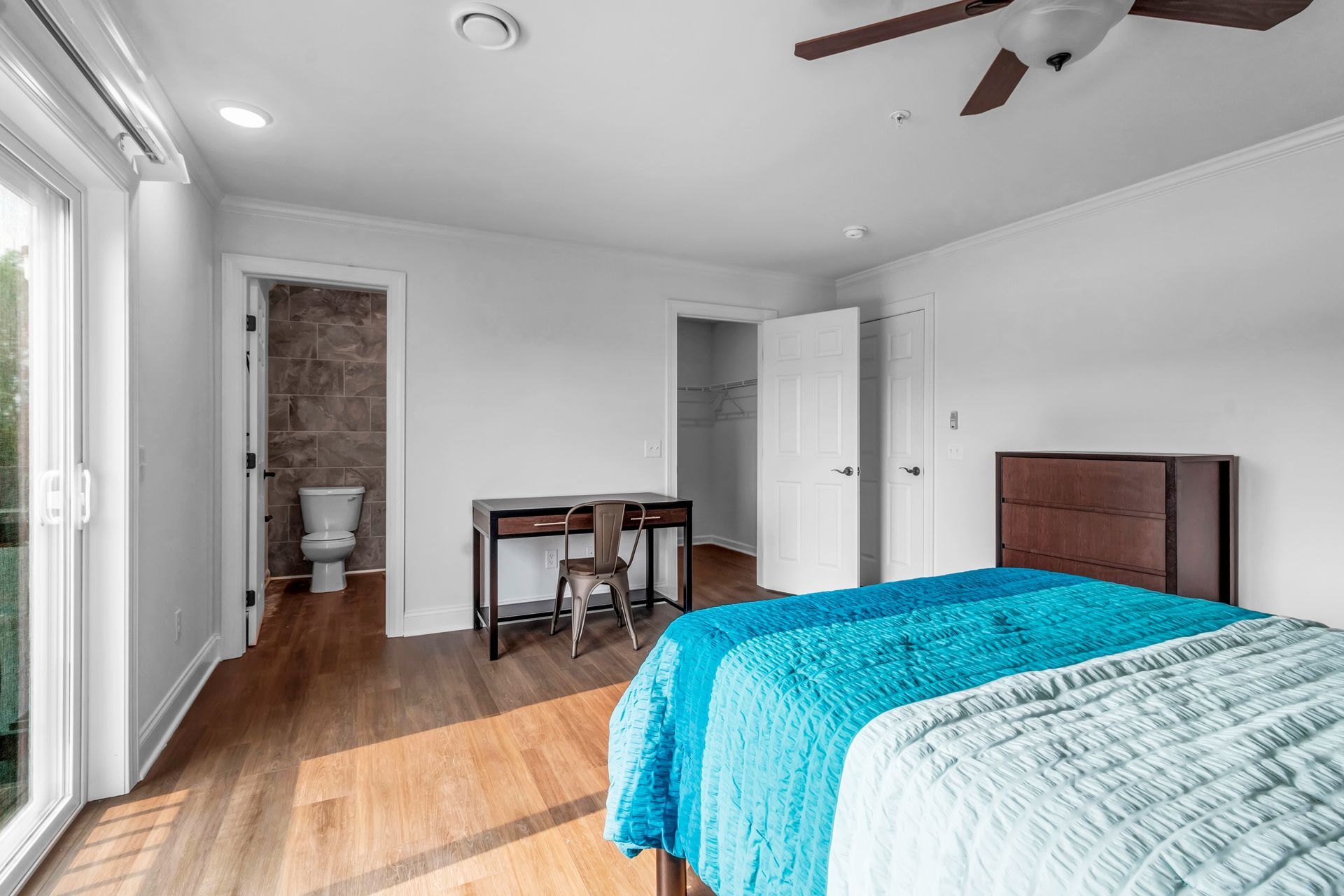 A bedroom with two beds , a desk , a toilet and a ceiling fan.