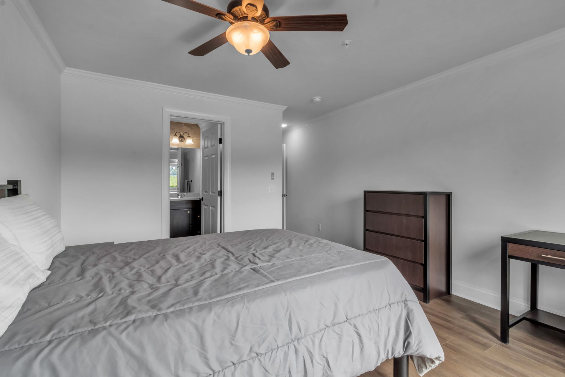 A bedroom with a bed , dresser , desk and ceiling fan.