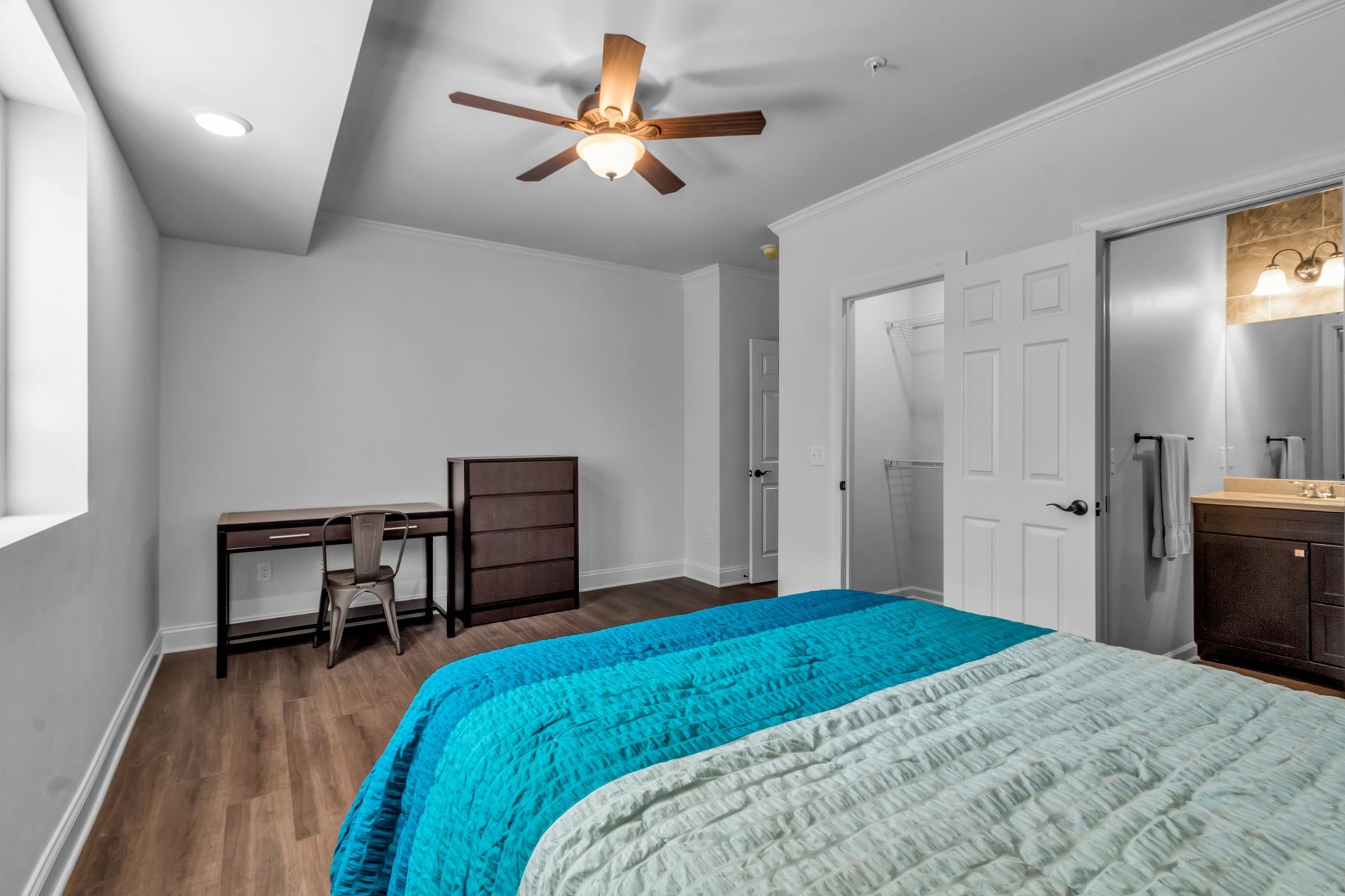 A bedroom with a bed , desk , dresser and ceiling fan.