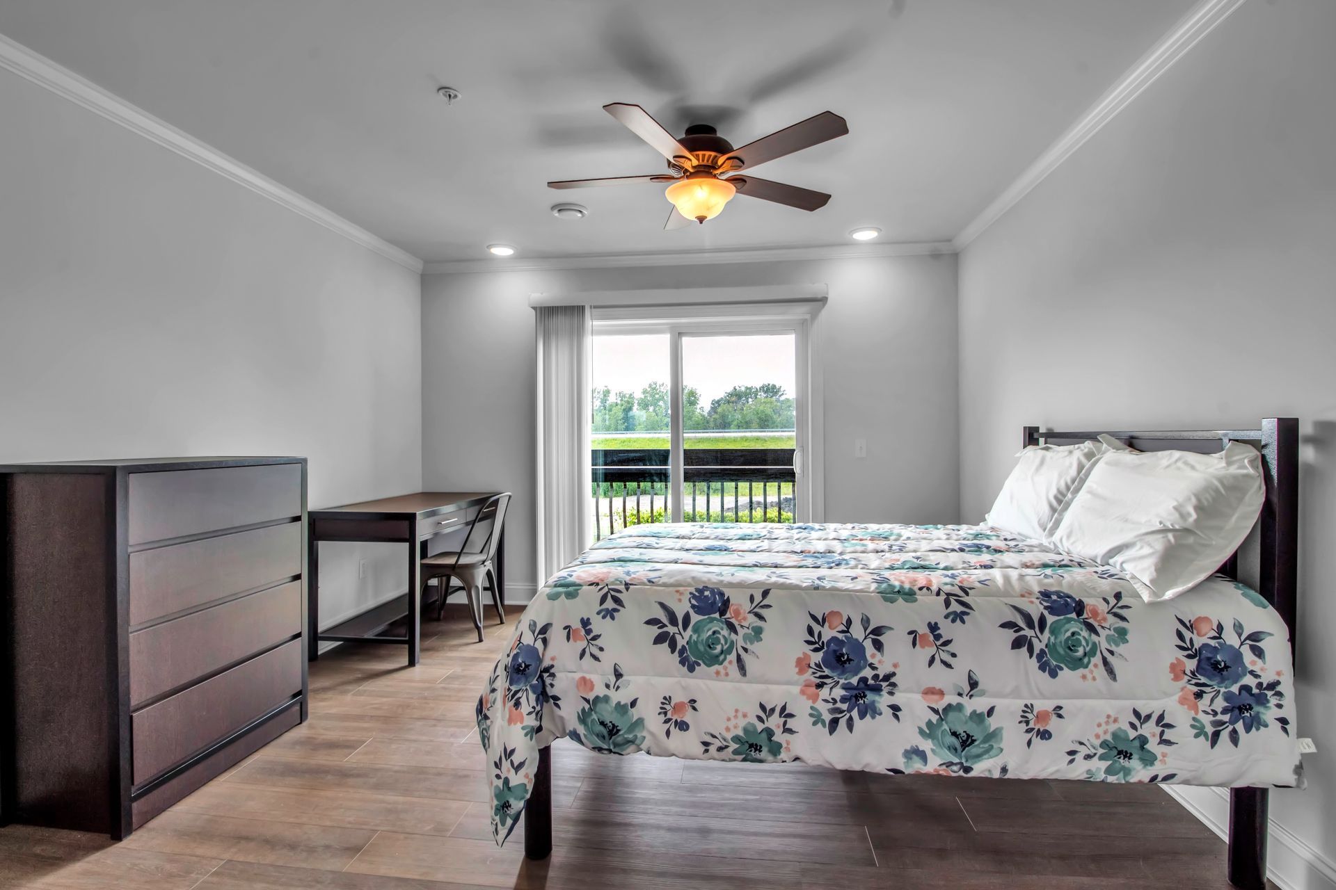 A bedroom with a bed , dresser , desk and ceiling fan.