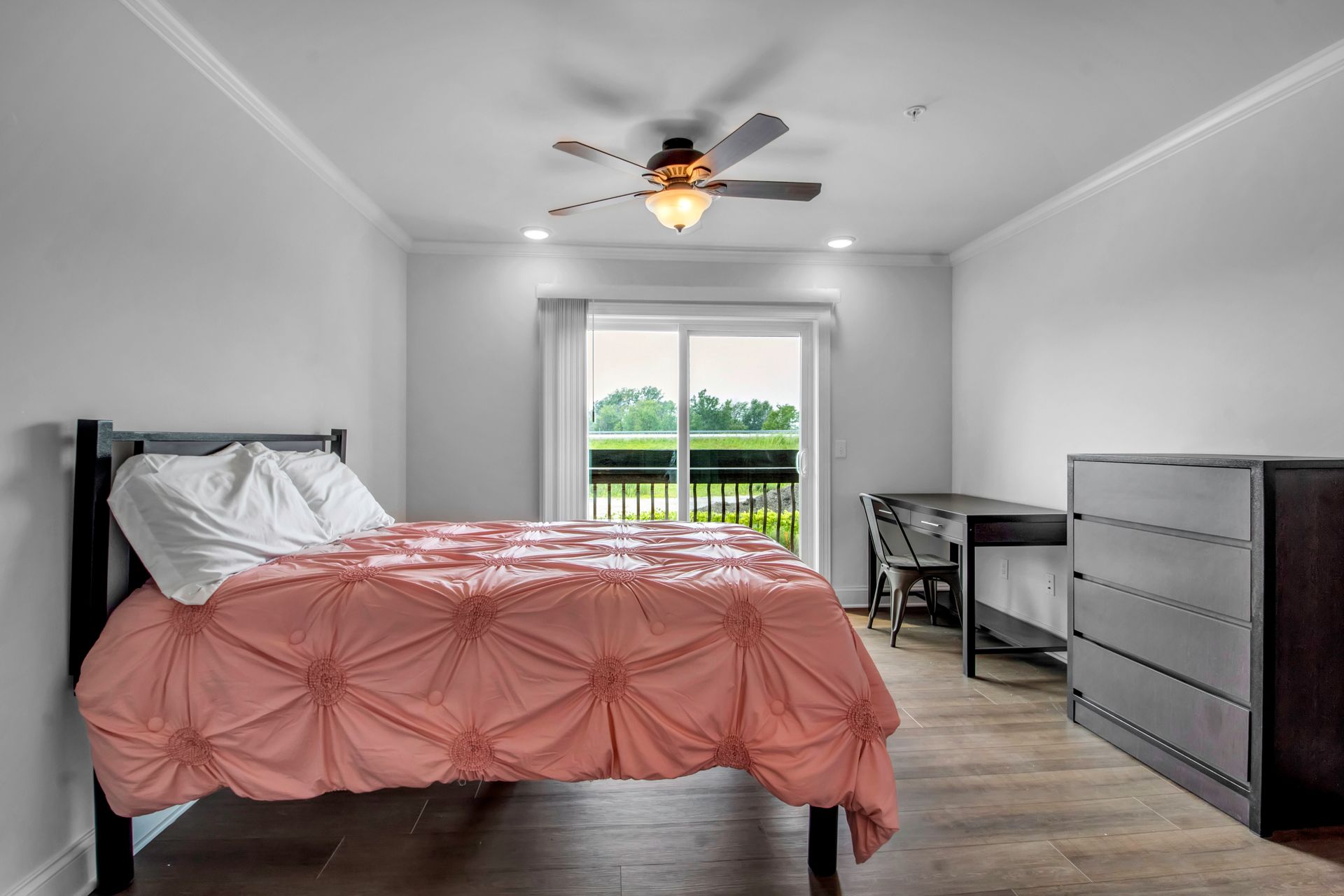A bedroom with a bed , dresser , desk and ceiling fan.