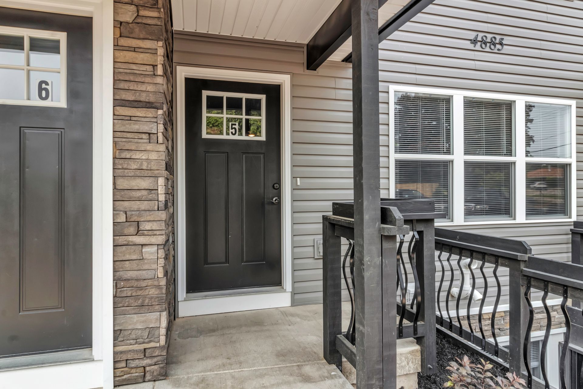 The front door of a house with a porch and a black door.