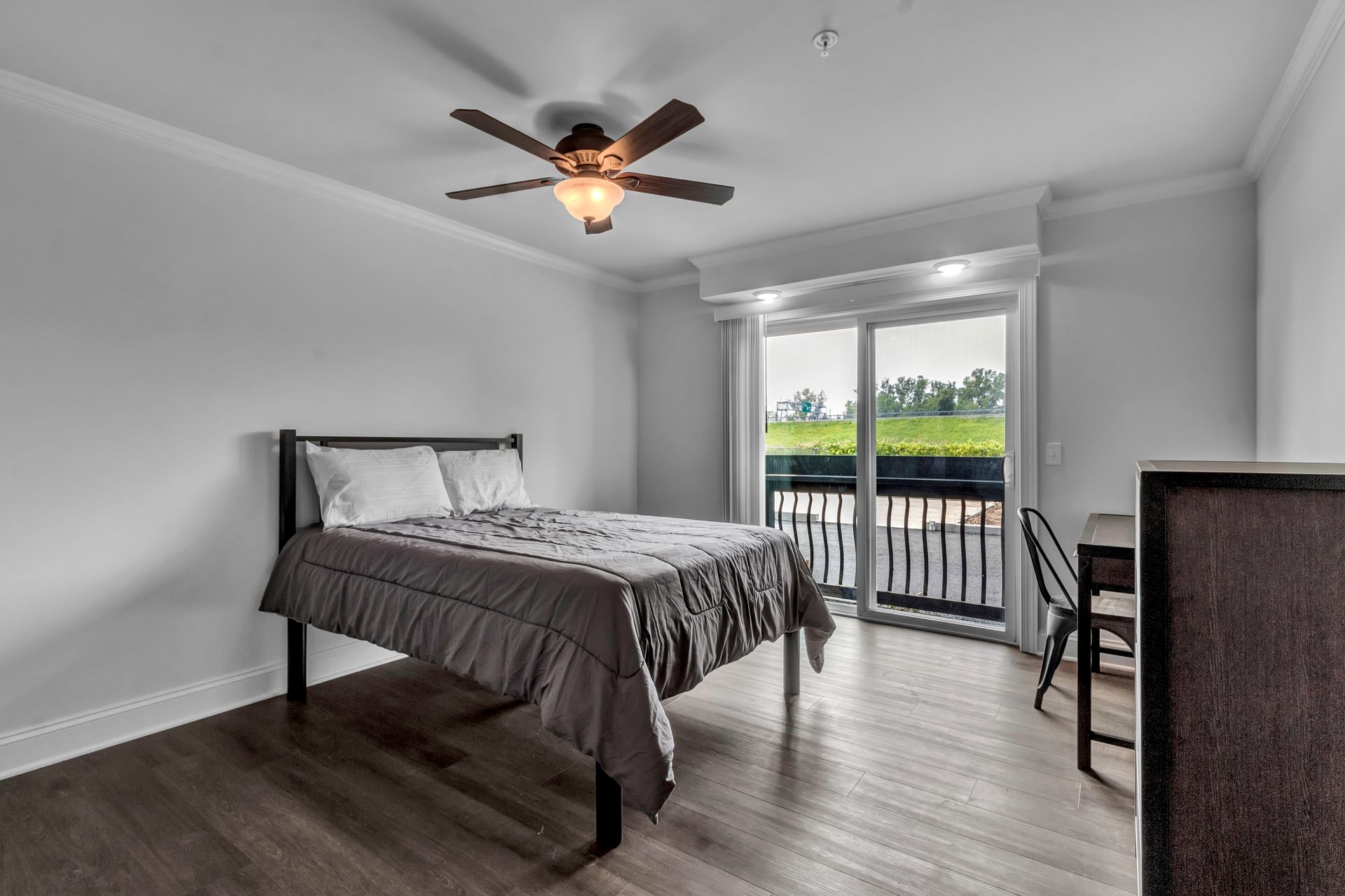 A bedroom with a bed , desk , chairs and a ceiling fan.