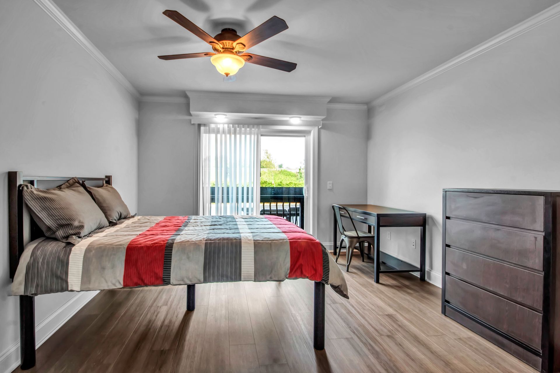 A bedroom with a bed , desk , dresser and ceiling fan.