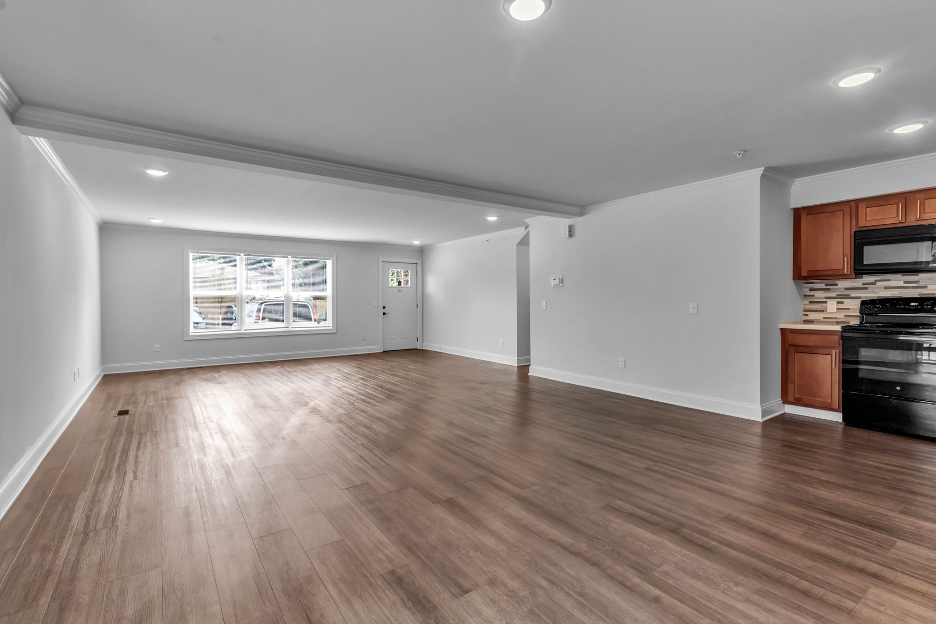 An empty living room with hardwood floors and a kitchen.