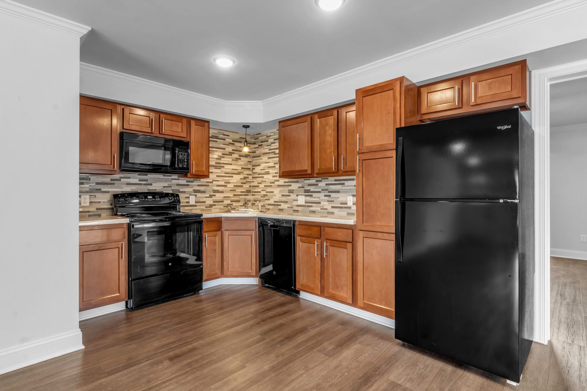 A kitchen with wooden cabinets , a black refrigerator , a stove , and a microwave.