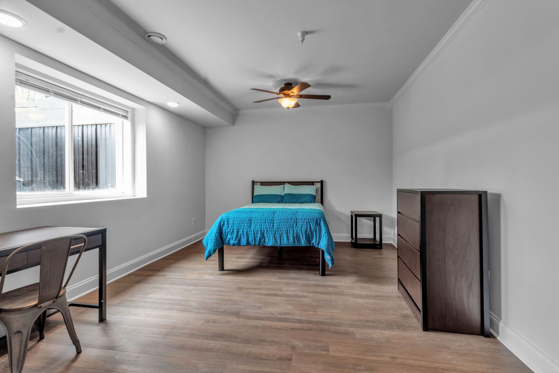 A bedroom with a bed , dresser , desk and ceiling fan.