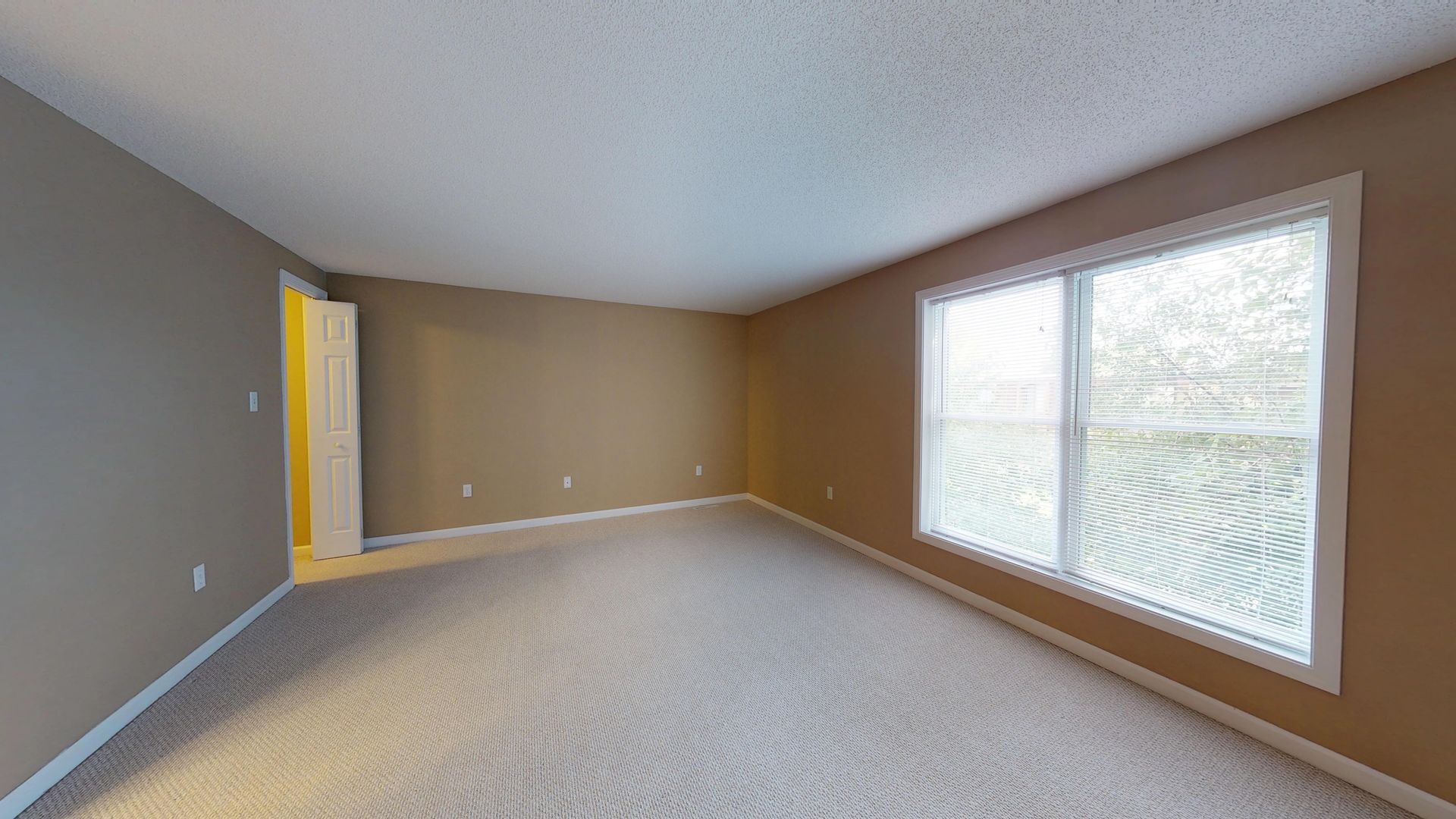 An empty living room with a large window and carpet.