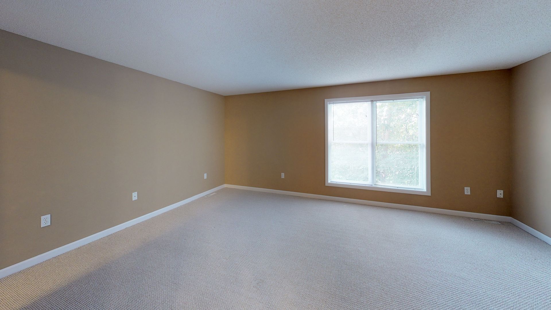 An empty living room with a large window and carpet.
