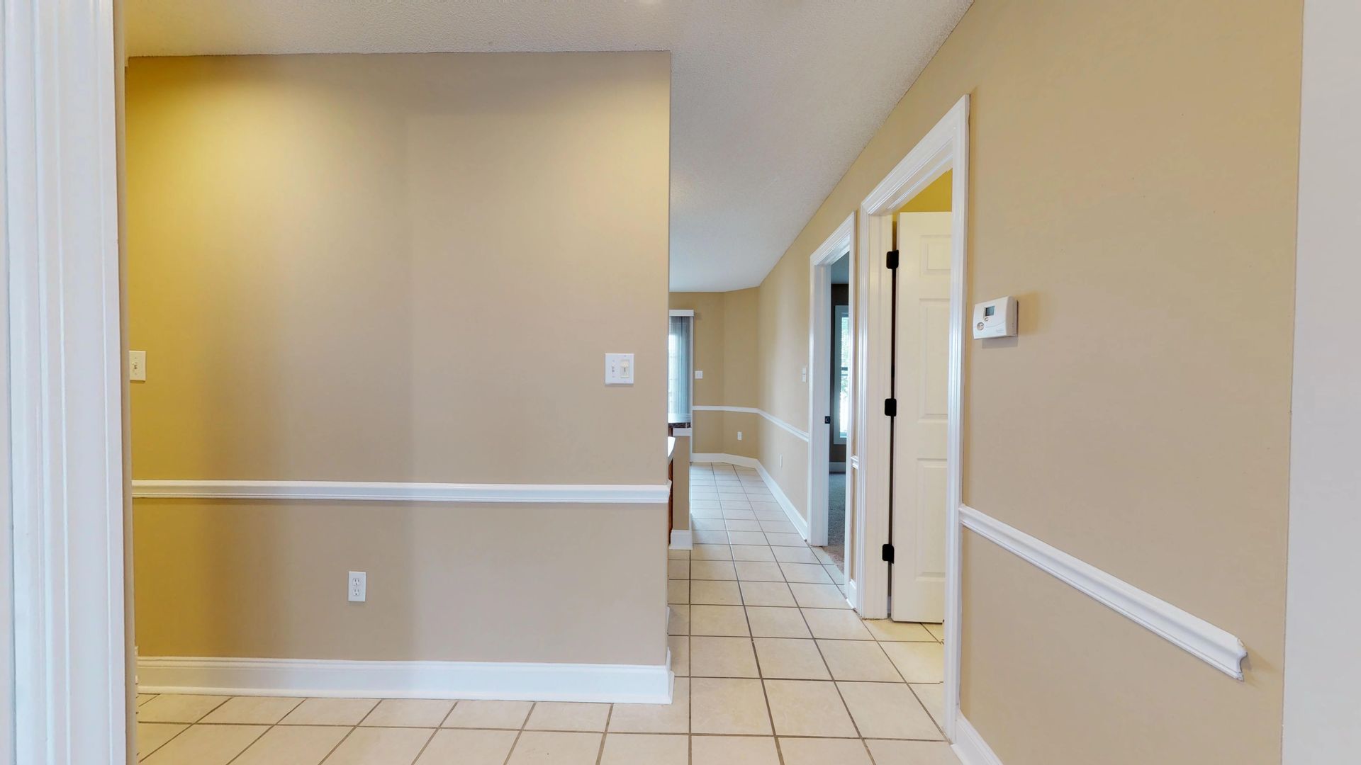 A hallway in a house with tile floors and beige walls.