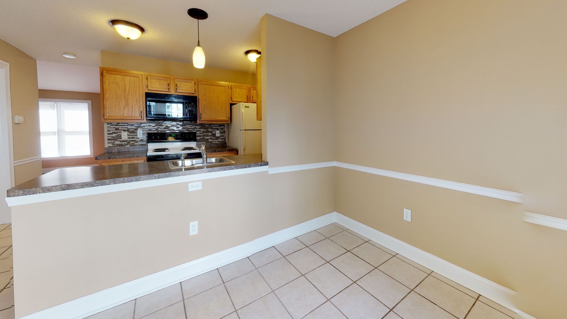 An empty dining room with a kitchen in the background.