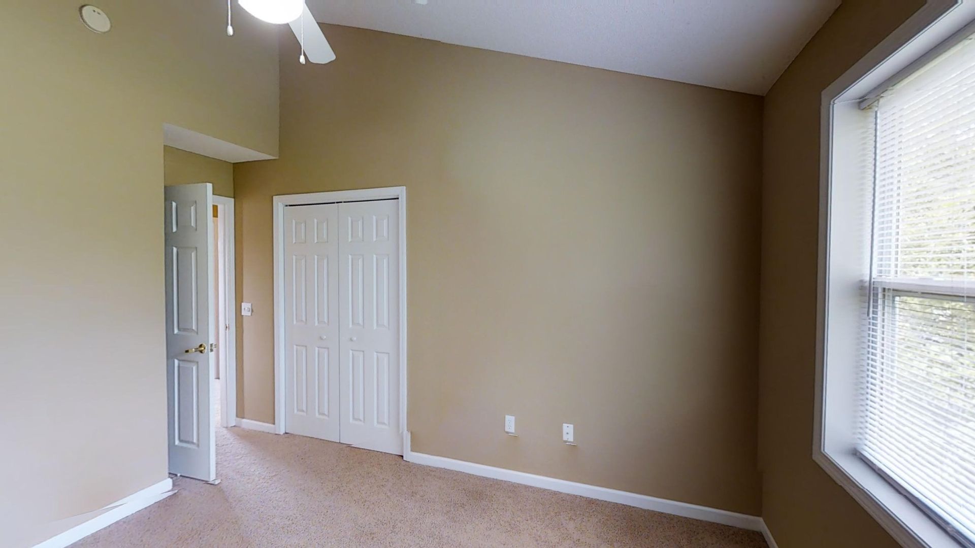 An empty bedroom with a ceiling fan and a window.