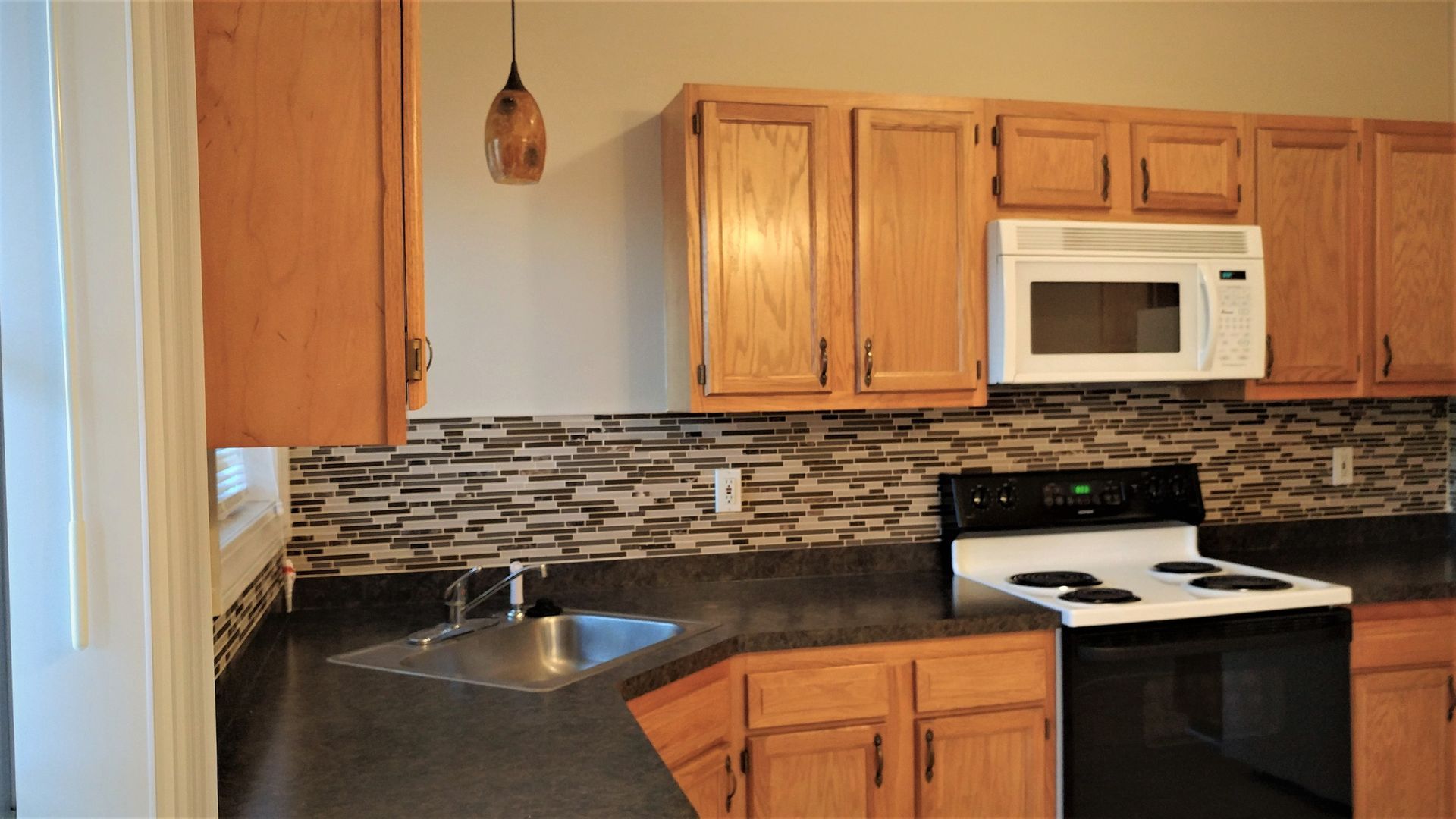 A kitchen with wooden cabinets , a stove , microwave and sink.